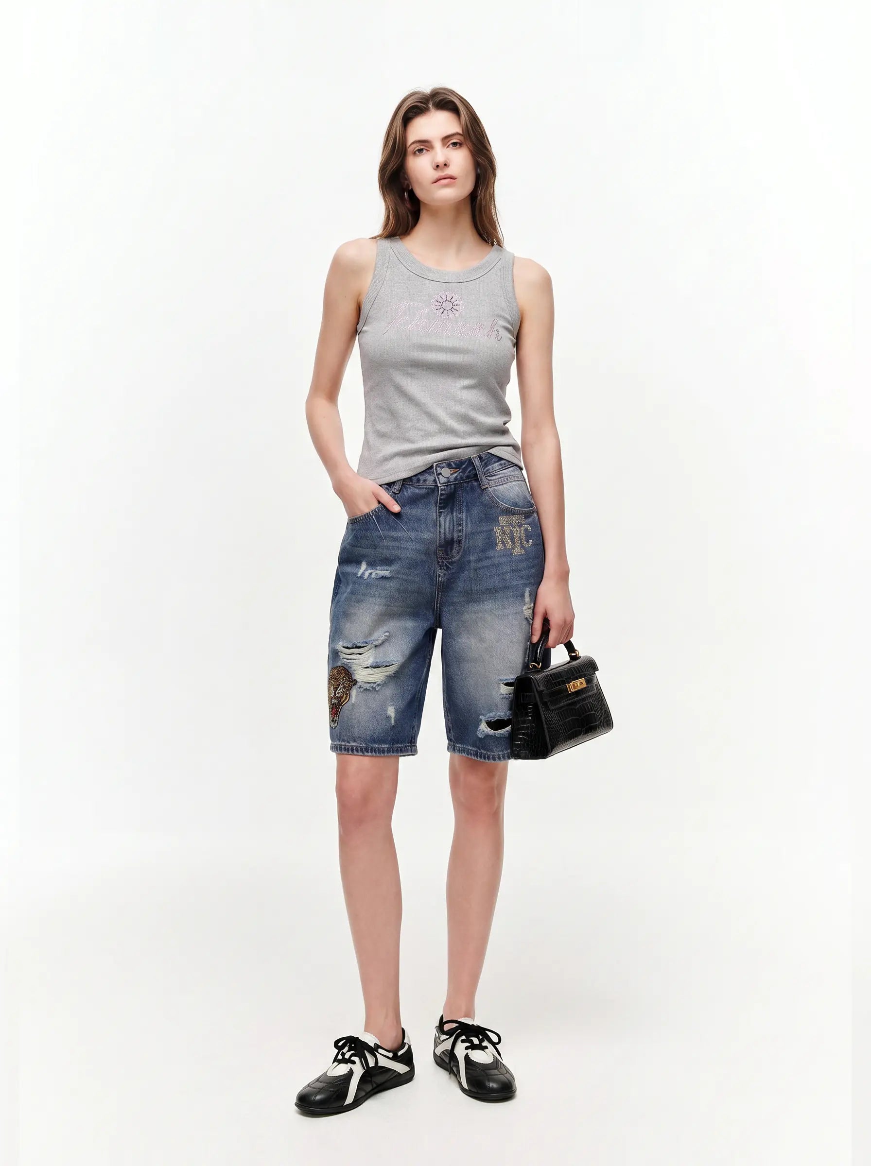 Woman wearing a gray tank top and blue denim shorts with patches, holding a black handbag on a white background. TCH Rhinestone Signature Ribbed Tank Top