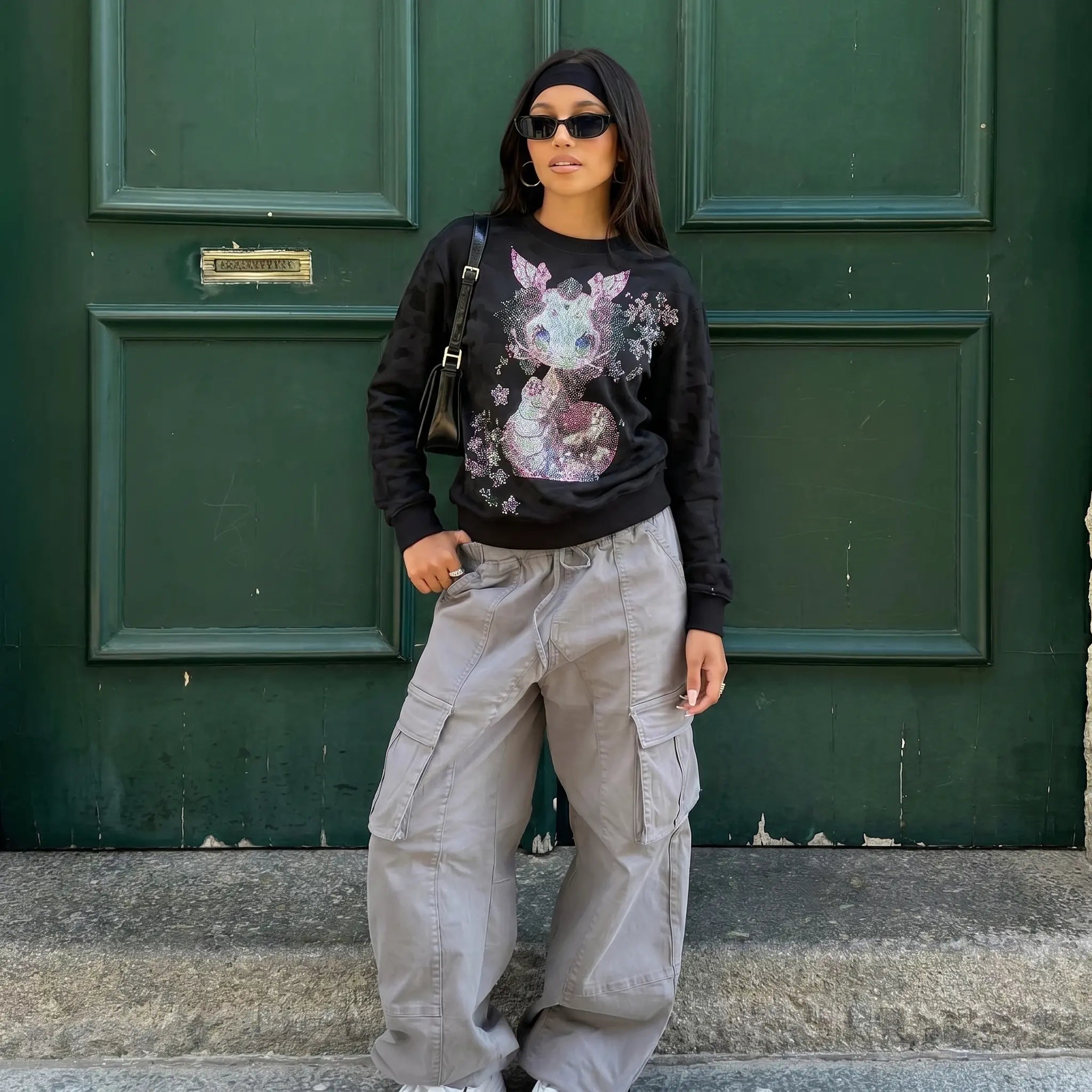 Person wearing a black sweatshirt with a colorful graphic and beige cargo pants standing in front of a green door. TCH Rhinestone Snake Black Crewneck Sweatshirt