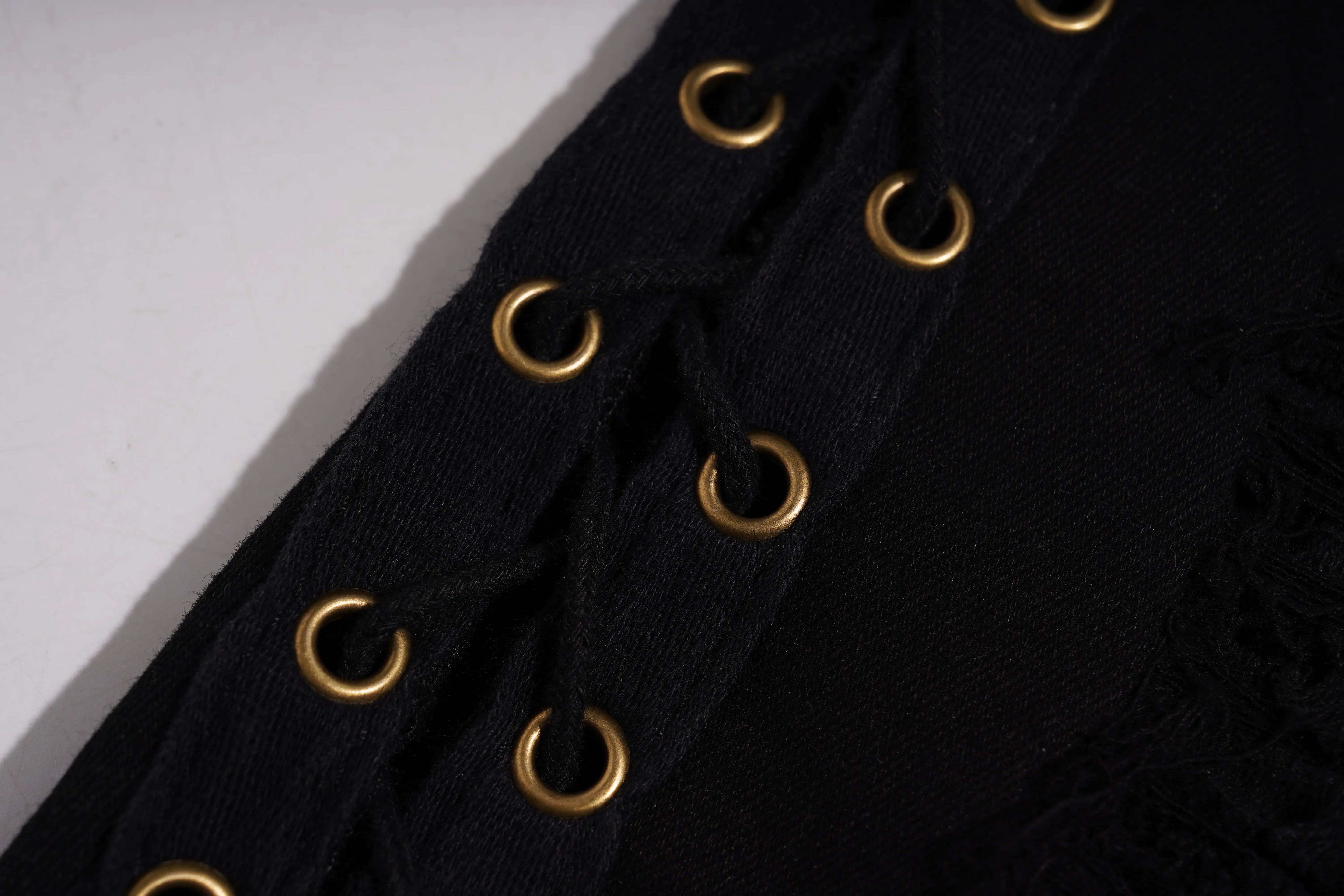 Close-up of a black lace-up garment featuring metallic gold eyelets and matching gold laces on a white background. TCH Rhinestone Sunflower Distressed Denim Shorts