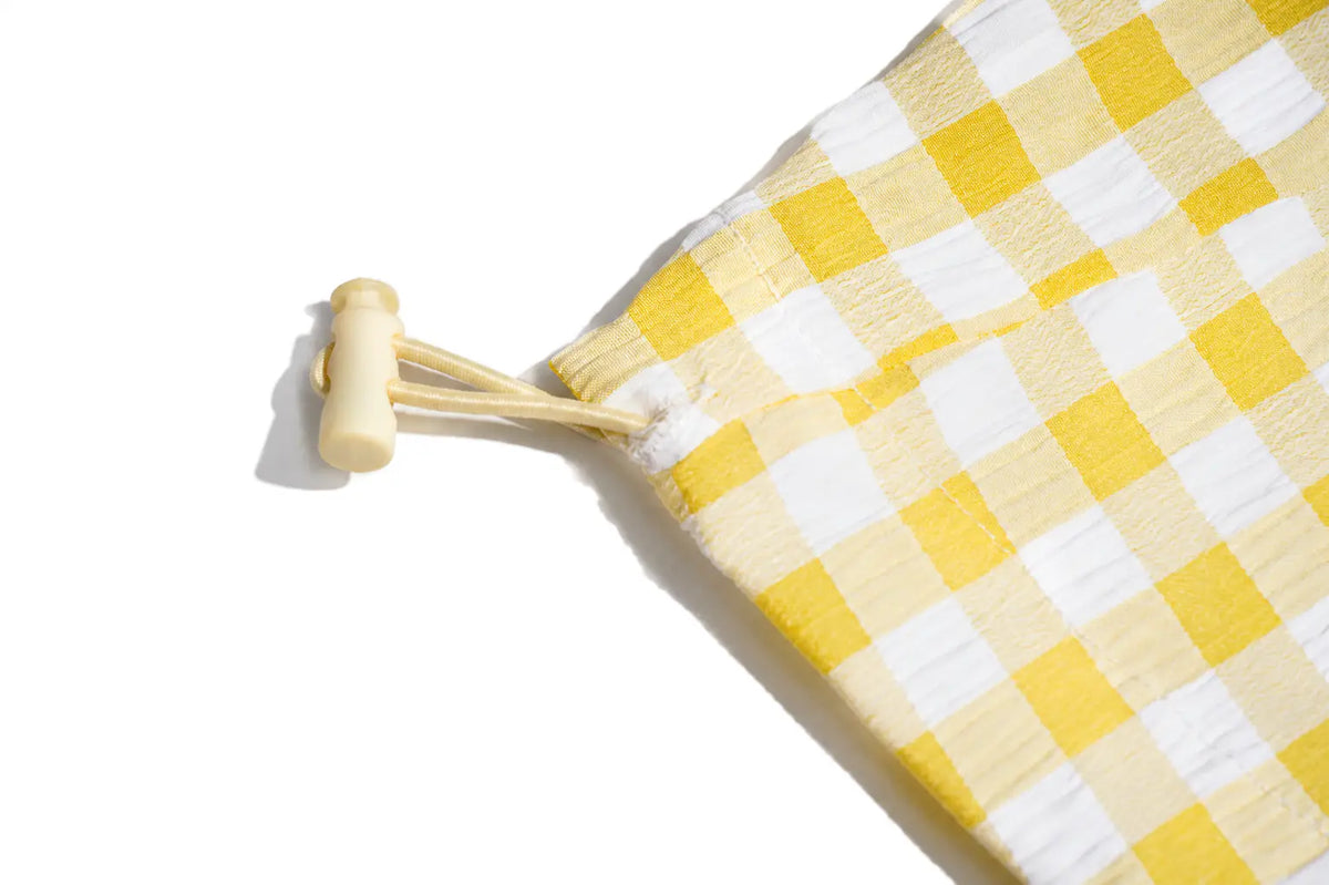 A close-up of a yellow and white gingham checkered fabric item with a light wood toggle and cord, photographed on a clean white background. TCH Rhinestone Sunflower Gingham Cargo Wide-Leg Pants
