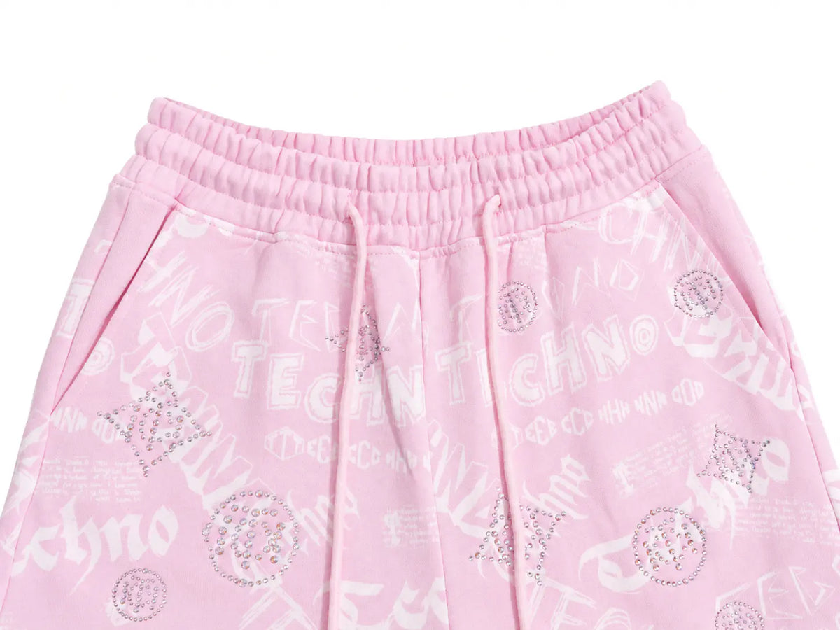 Pink sweatpants with a white 'TECHNO' graphic print and rhinestone embellishments, featuring an elastic waistband and drawstrings. TCH Rhinestone Techno Graphic Wide-Leg Sweatpants
