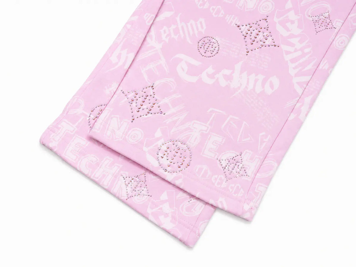 A close-up of a light pink textile, likely a bandana or scarf, featuring a white 'Techno' graphic pattern with rhinestone embellishments. TCH Rhinestone Techno Graphic Wide-Leg Sweatpants