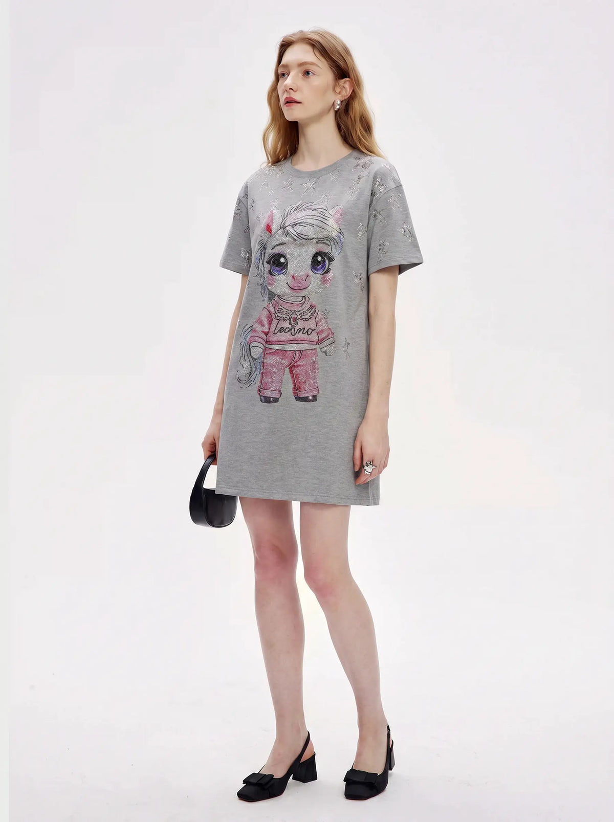 A woman modeling a gray short-sleeve t-shirt dress featuring a cartoon unicorn graphic on the front, styled with black heels and a small black handbag against a plain white studio background. TCH Rhinestone Techno Unicorn Graphic T-Shirt