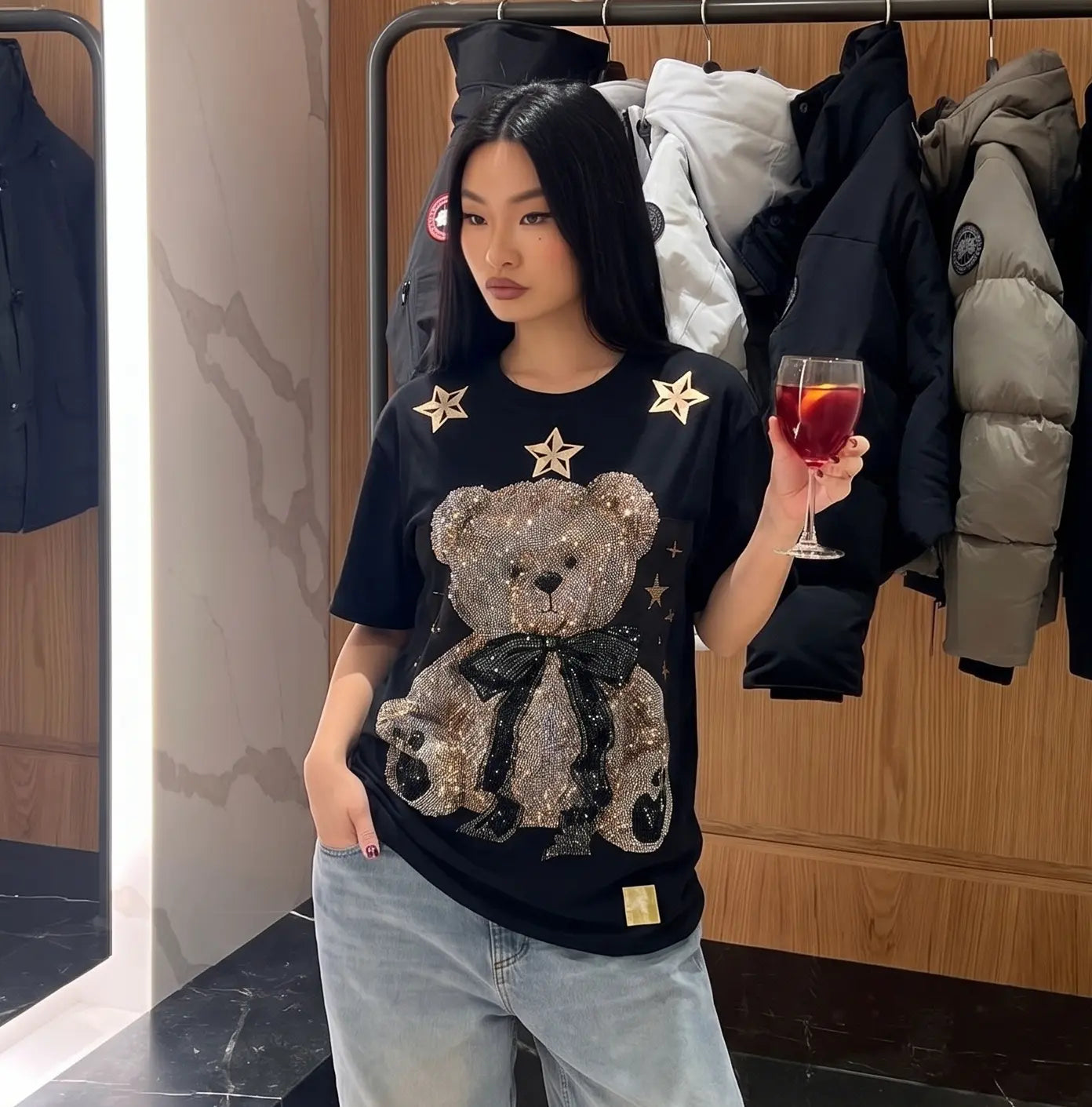 Woman wearing a black t-shirt with a teddy bear design, holding a glass of red wine in a clothing store. TCH Rhinestone Teddy Bear Black T-Shirt