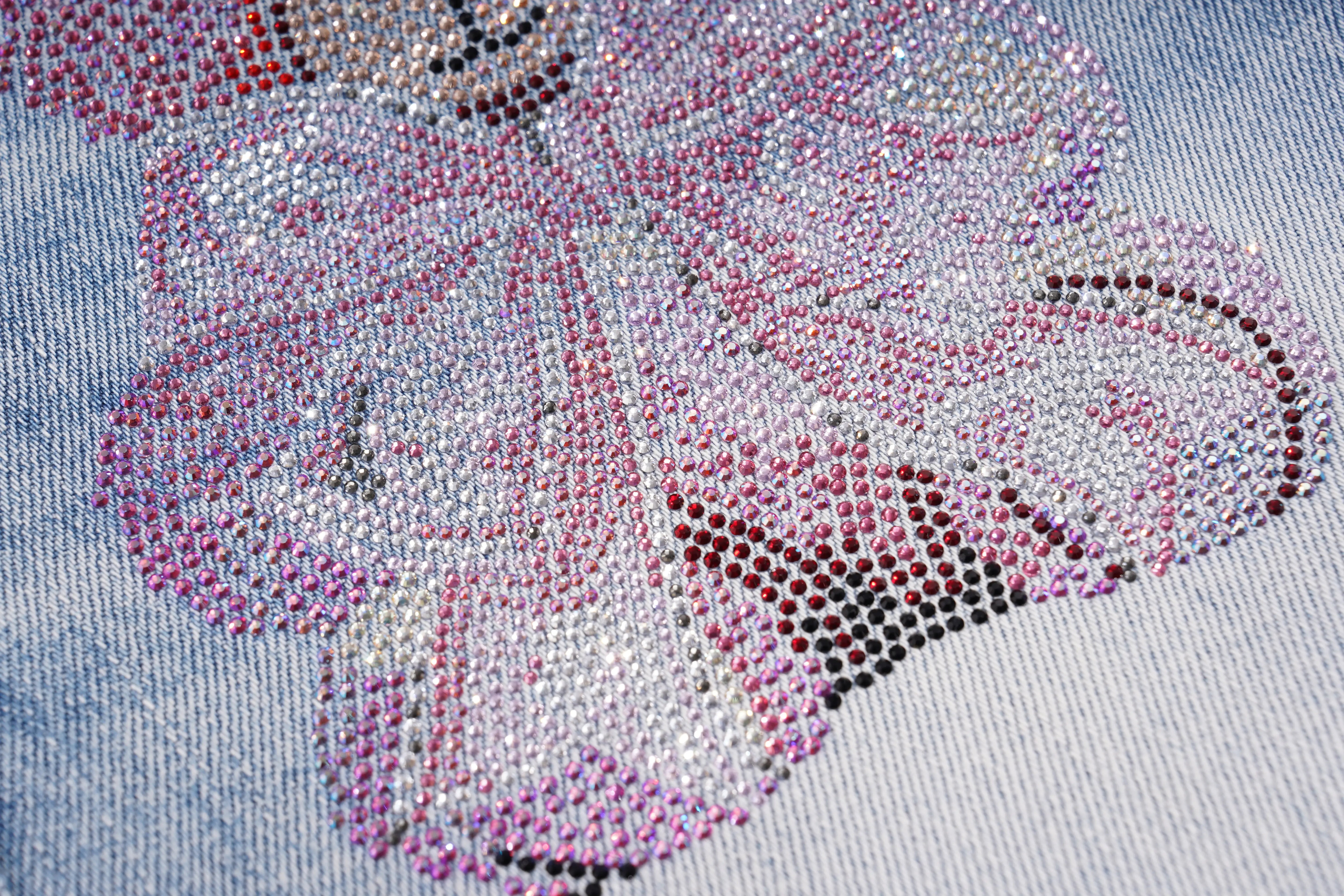 A close-up of a rhinestone-embellished floral applique on light blue denim fabric, featuring pink, silver, and dark metallic rhinestones. TCH Rhinestone Teddy Bear Bow Denim Shorts