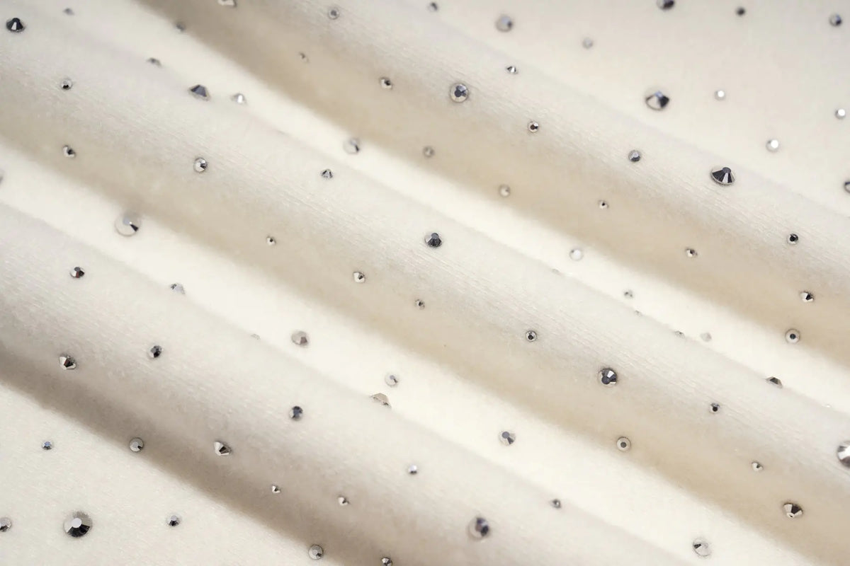 Close-up of a cream-colored fabric with small, evenly spaced silver rhinestones or studs, arranged in soft diagonal folds. TCH Rhinestone Teddy Bear Bow Graphic Cropped T-Shirt