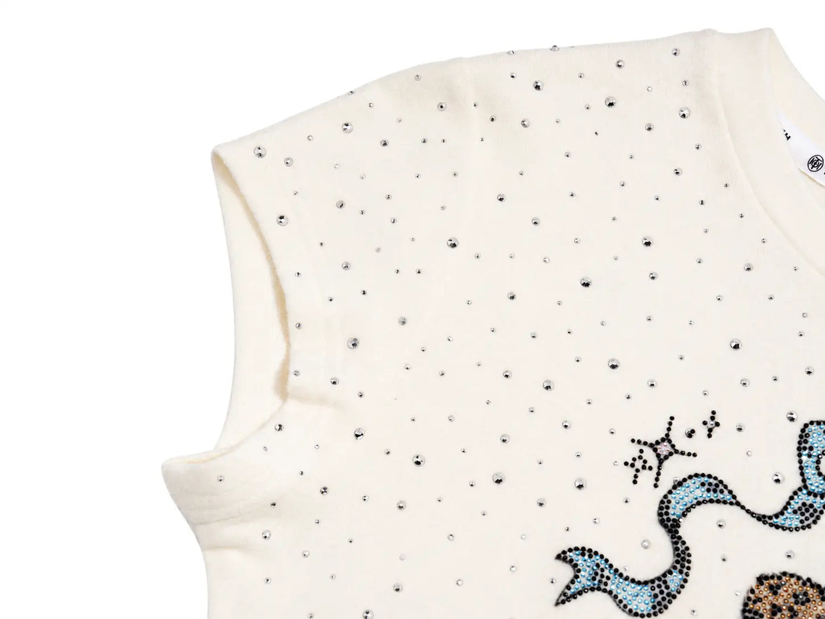 Close-up of a cream-colored sleeveless top or dress featuring a scattered pattern of small black rhinestones and a partial blue and brown sequined graphic on the lower right, set against a plain white background. TCH Rhinestone Teddy Bear Bow Graphic Cropped T-Shirt
