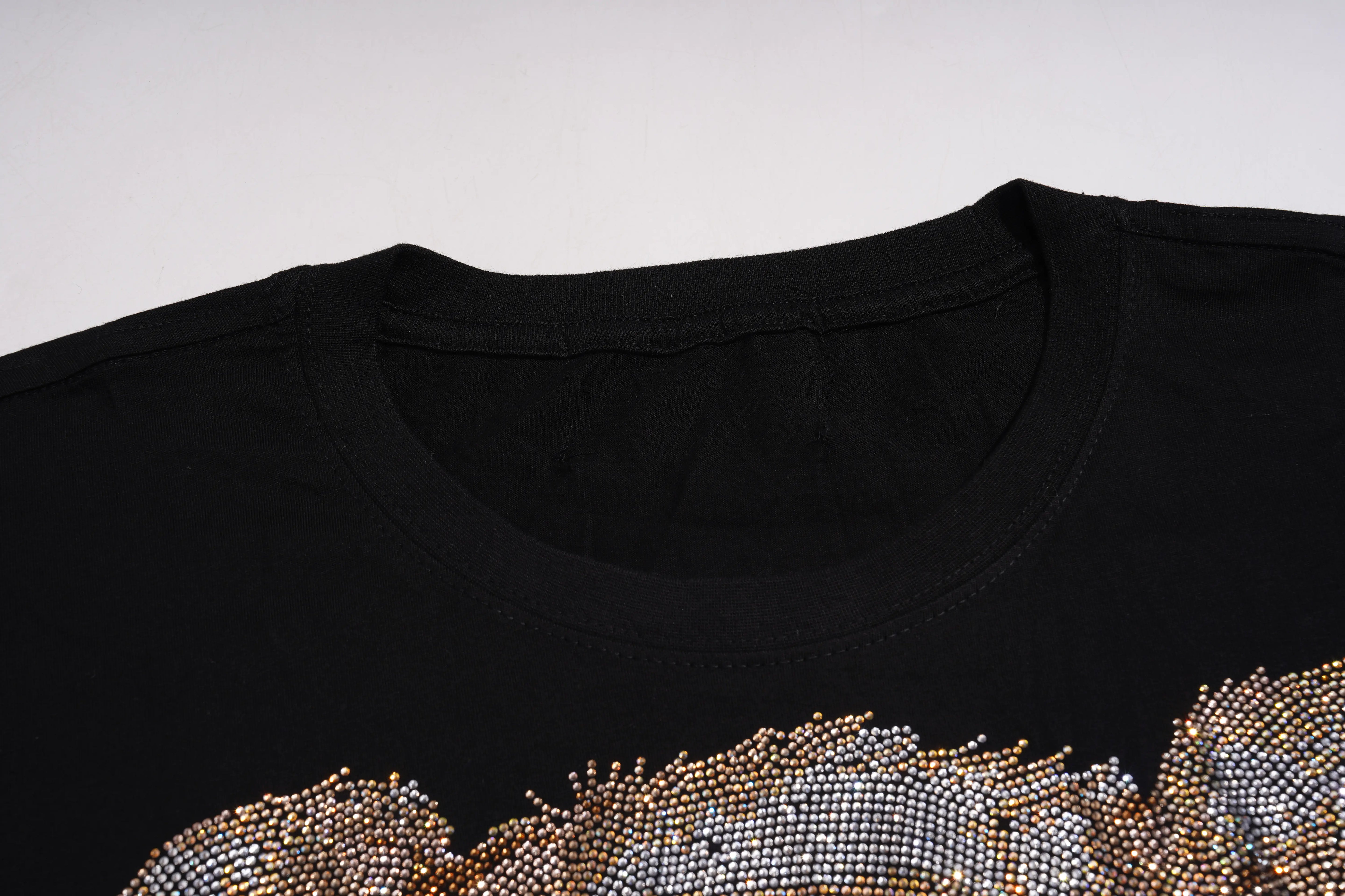 Close-up of a black crewneck t-shirt featuring a large, textured graphic at the bottom made of shimmering rhinestones in gold, silver, and white. TCH Rhinestone Teddy Bear Bow Graphic Oversized Black T-Shirt
