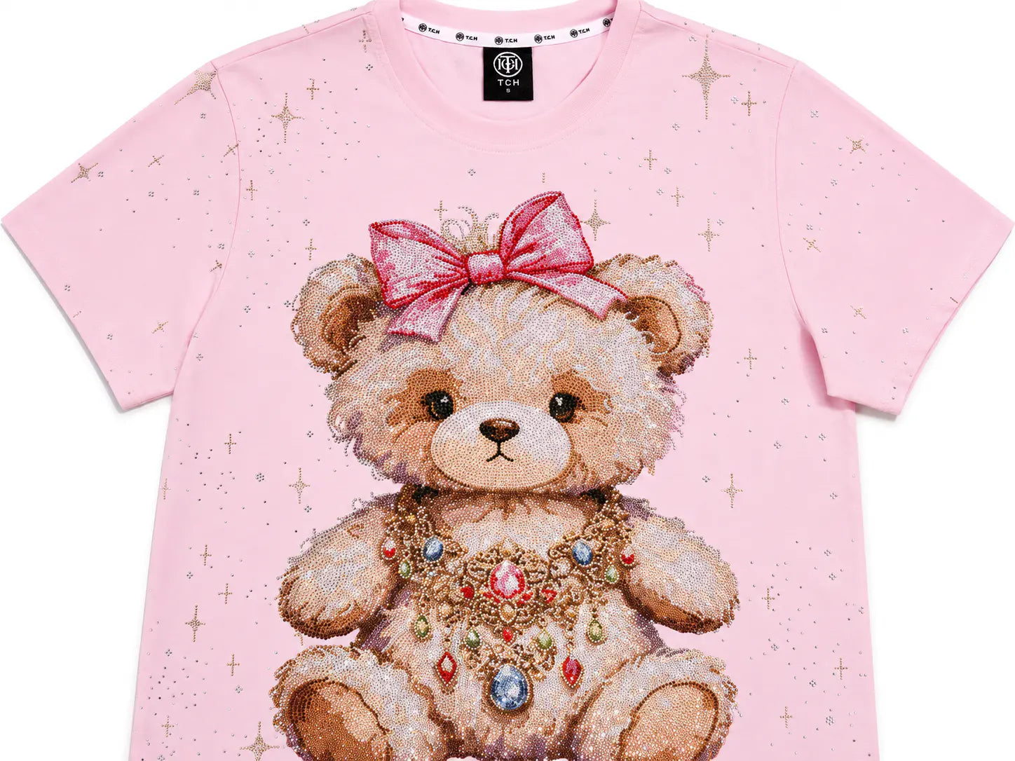 A light pink short-sleeve t-shirt featuring a large graphic of a teddy bear wearing a pink bow and a jeweled necklace, with subtle gold star details scattered across the fabric. TCH Rhinestone Teddy Bear Bow Pink Graphic T-Shirt