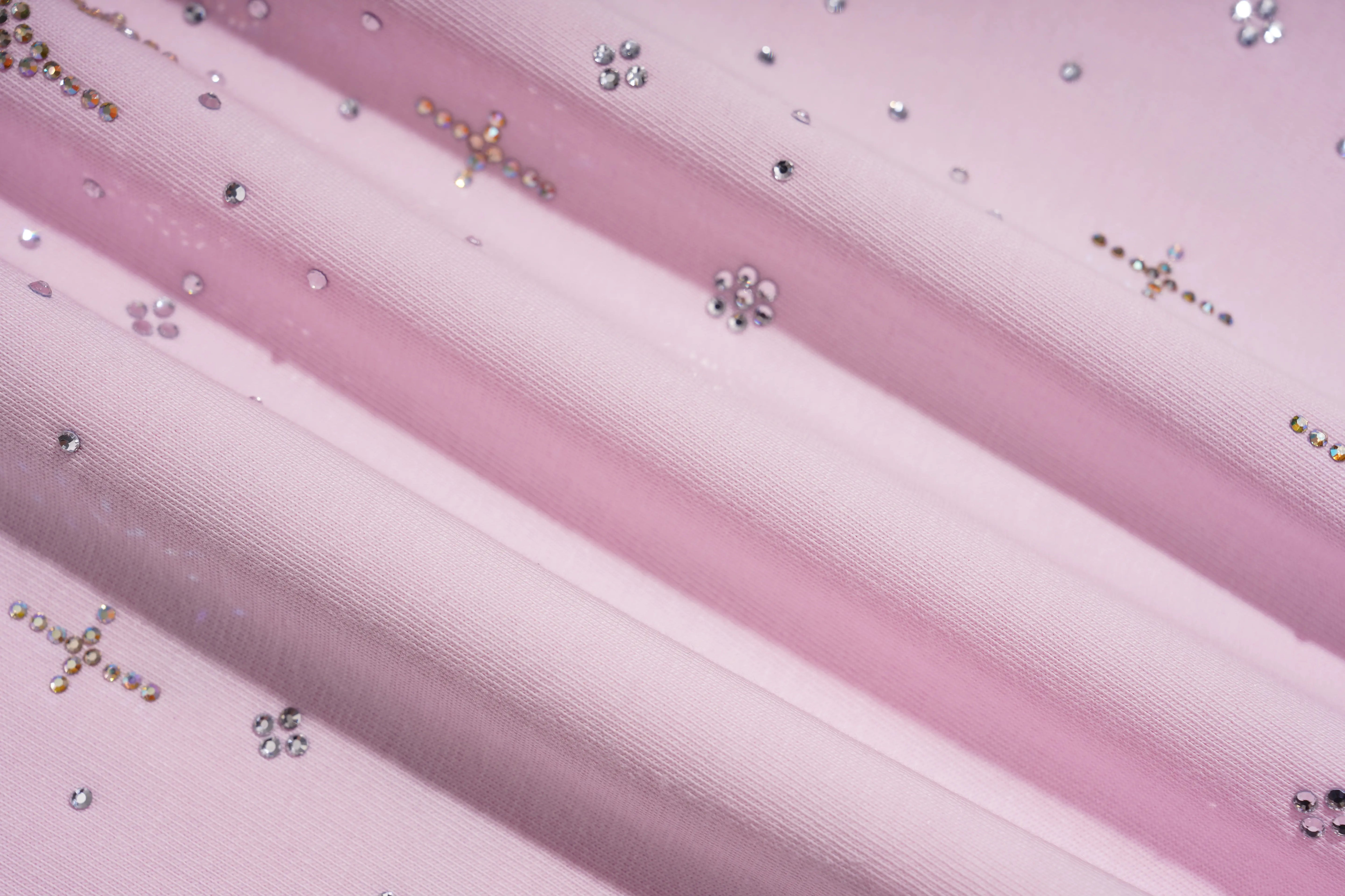 A close-up of light pink satin fabric with diagonal folds and scattered small silver rhinestones. TCH Rhinestone Teddy Bear Bow Pink Graphic T-Shirt