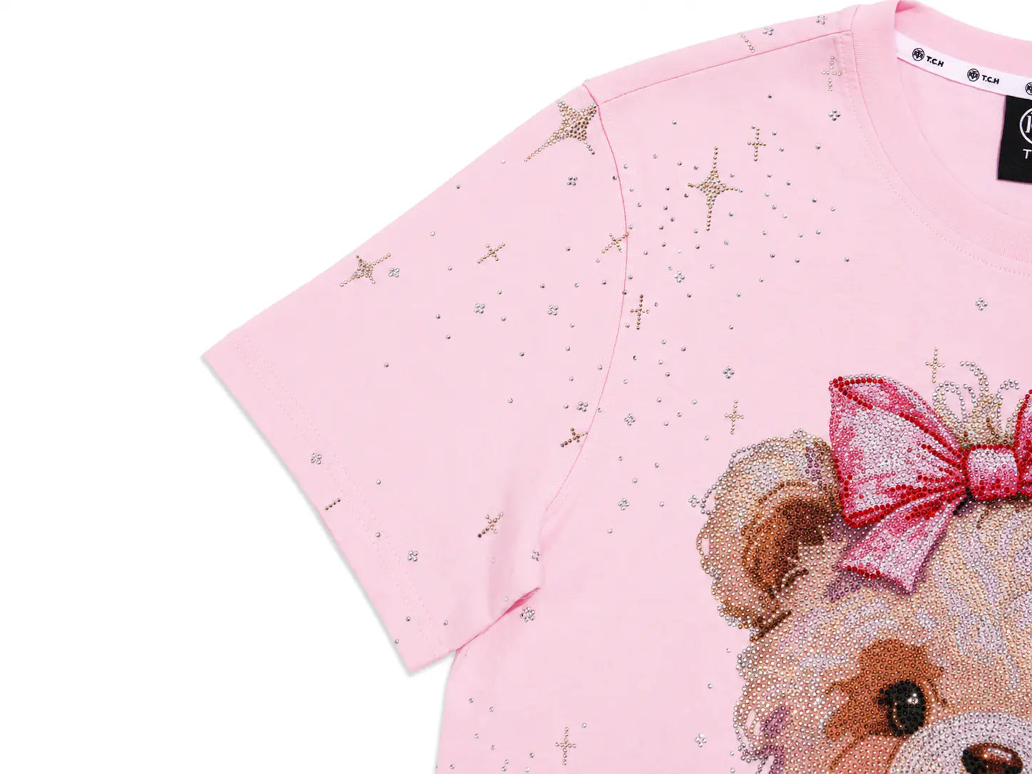A close-up of a light pink short-sleeve t-shirt featuring a beaded teddy bear graphic on the front with a pink sequined bow and scattered rhinestone star accents. TCH Rhinestone Teddy Bear Bow Pink Graphic T-Shirt