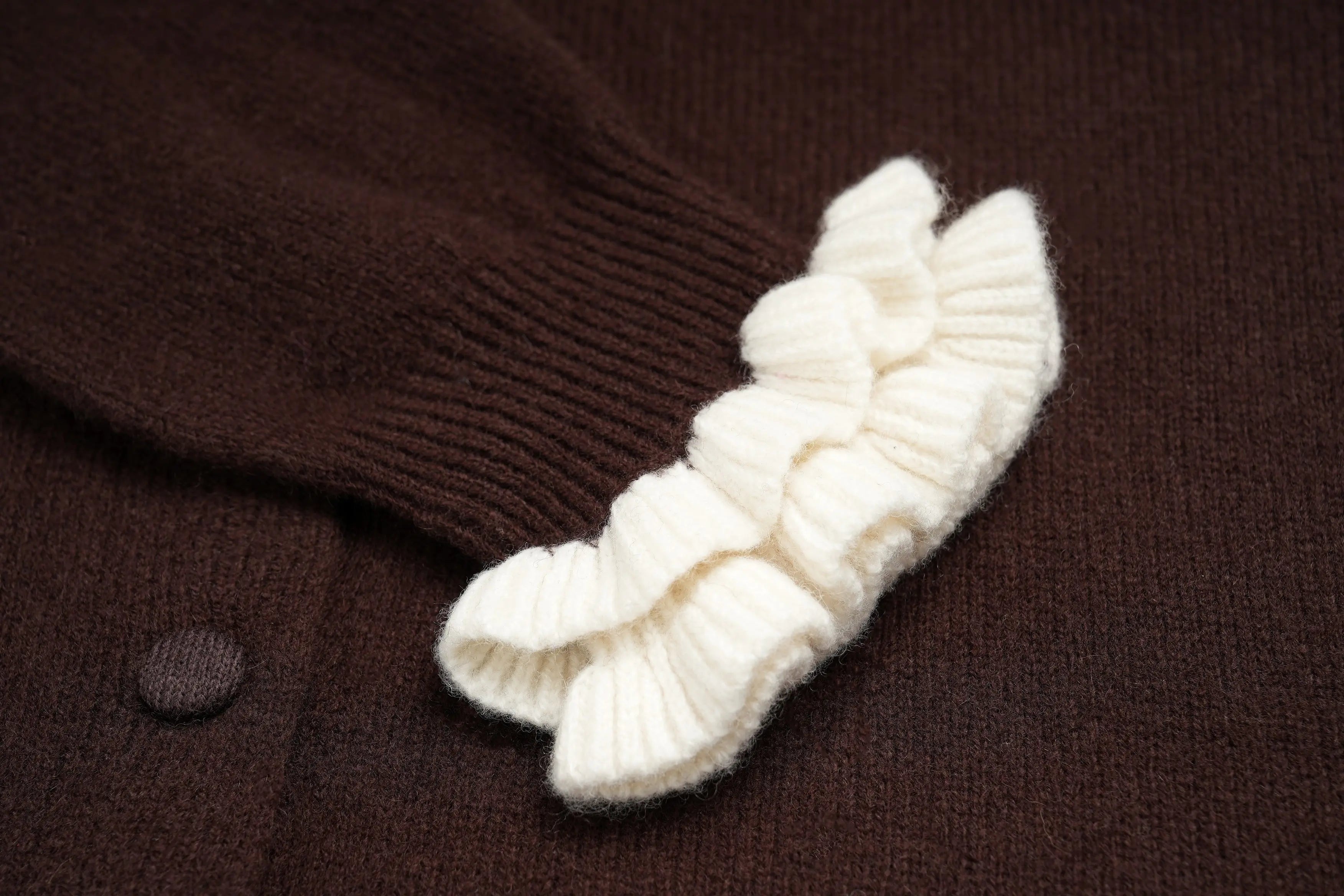 Close-up of a dark brown knit cardigan featuring a decorative cream-colored ruffled trim along the sleeve cuff. TCH Rhinestone Teddy Bear Bow Ruffle Knit Cardigan