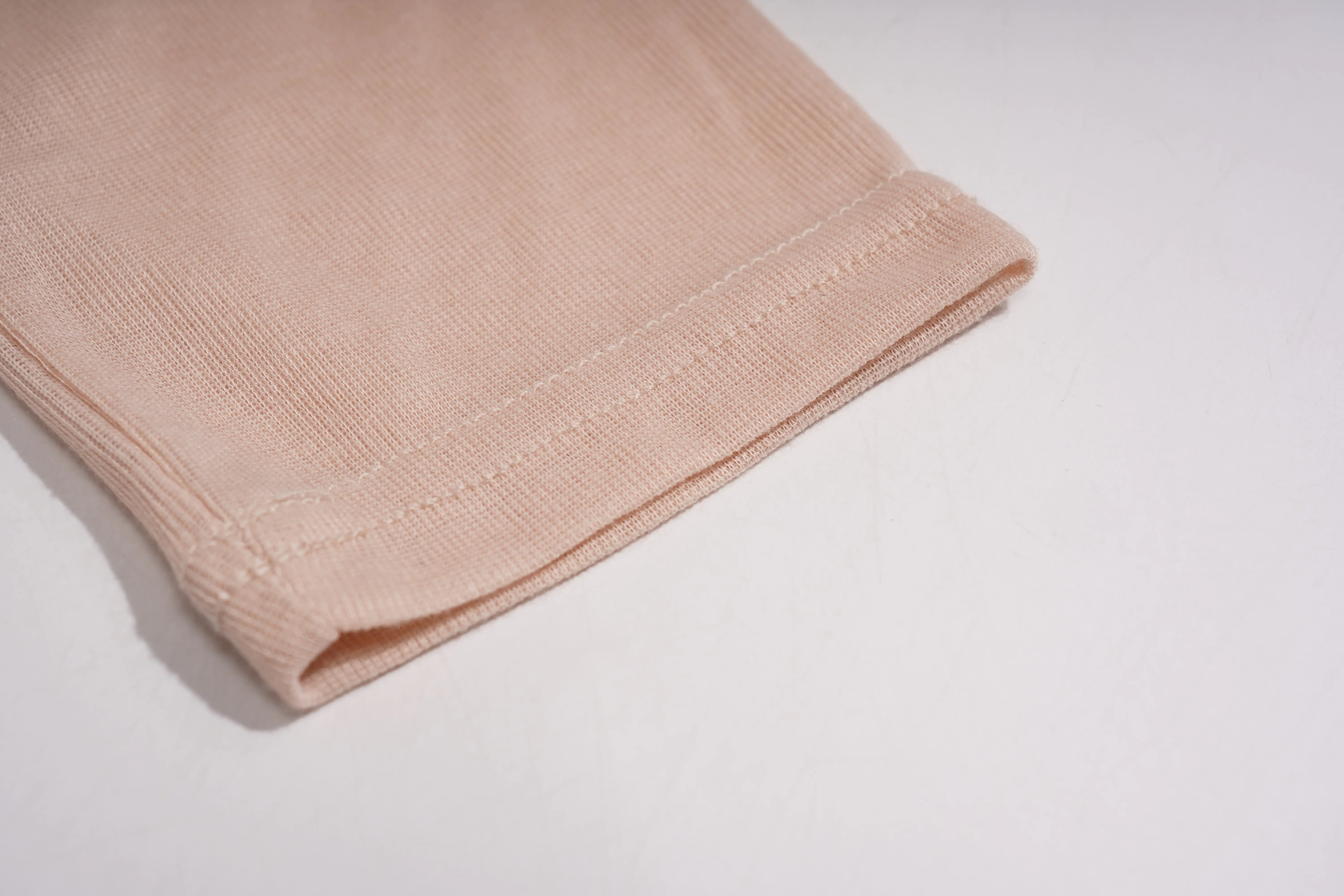 A close-up of a folded ribbed knit fabric in a light peach-beige color, showing the texture and hem stitching on a plain white background. TCH Rhinestone Teddy Bear Bow Ruffle Long Sleeve Top