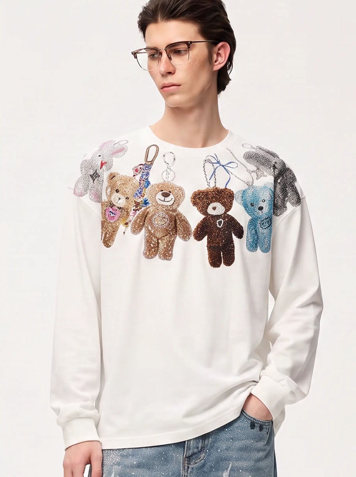 A model wearing a light blue denim jacket with various embroidered patches, including a teddy bear on the left chest and cherries on the sleeve, styled over a white t-shirt and dark pants. TCH Rhinestone Teddy Bear Charm Graphic Long Sleeve Sweatshirt