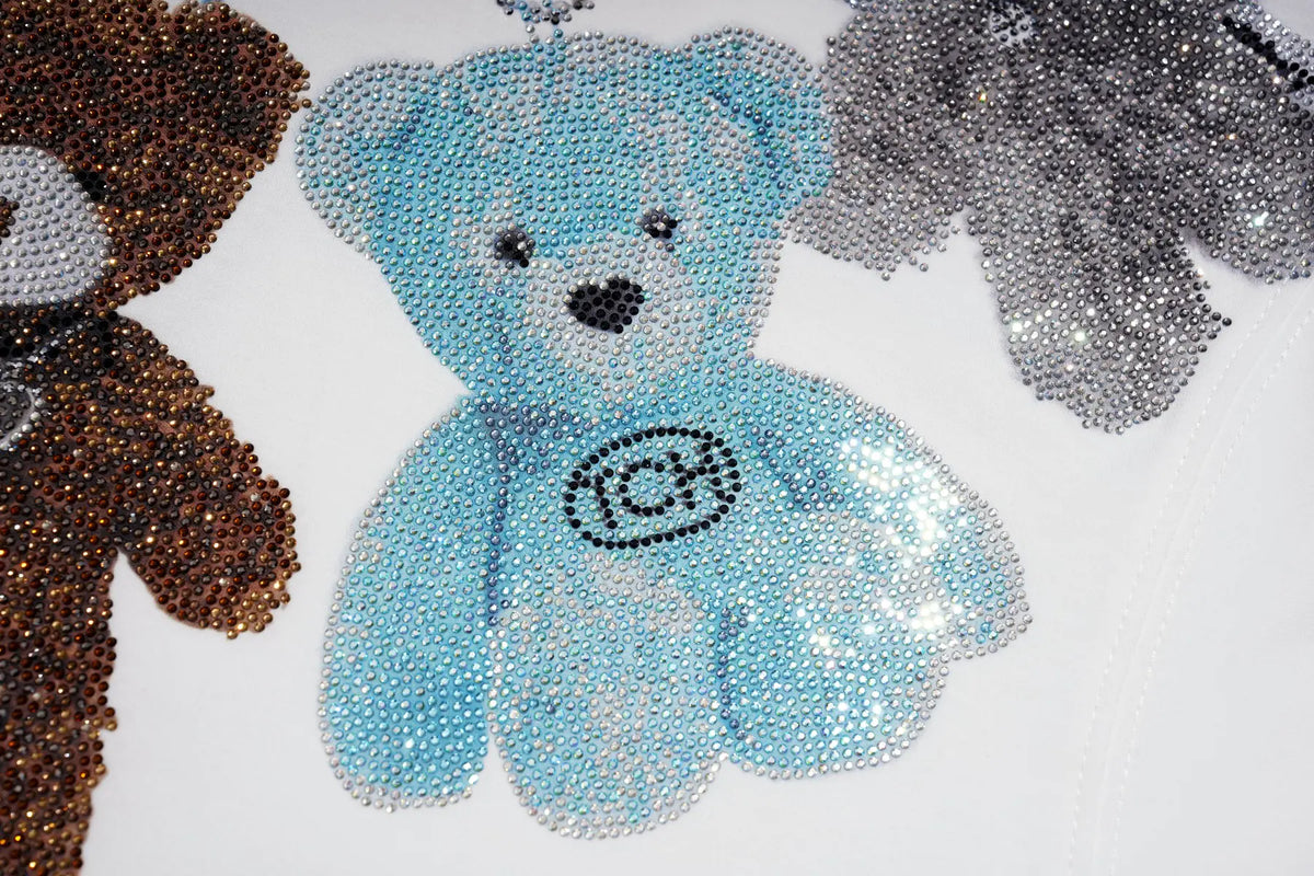 A close-up of a light blue rhinestone teddy bear applique or patch on a white background, with partial brown and silver versions visible at the edges. TCH Rhinestone Teddy Bear Charm Graphic Long Sleeve Sweatshirt