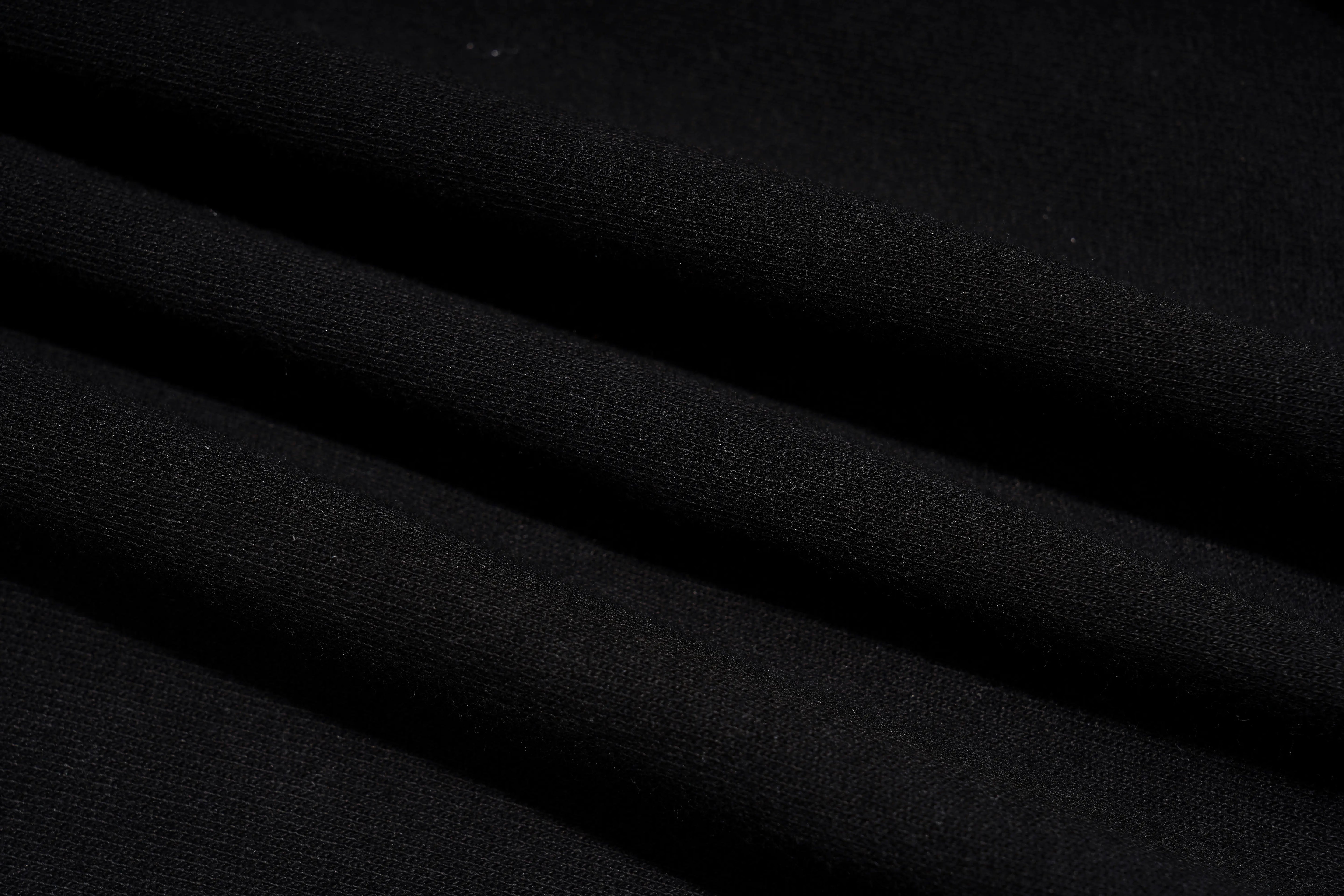 A close-up of draped black fabric with soft diagonal folds showing a fine knit texture. TCH Rhinestone Teddy Bear Graphic Black Jogger Pants