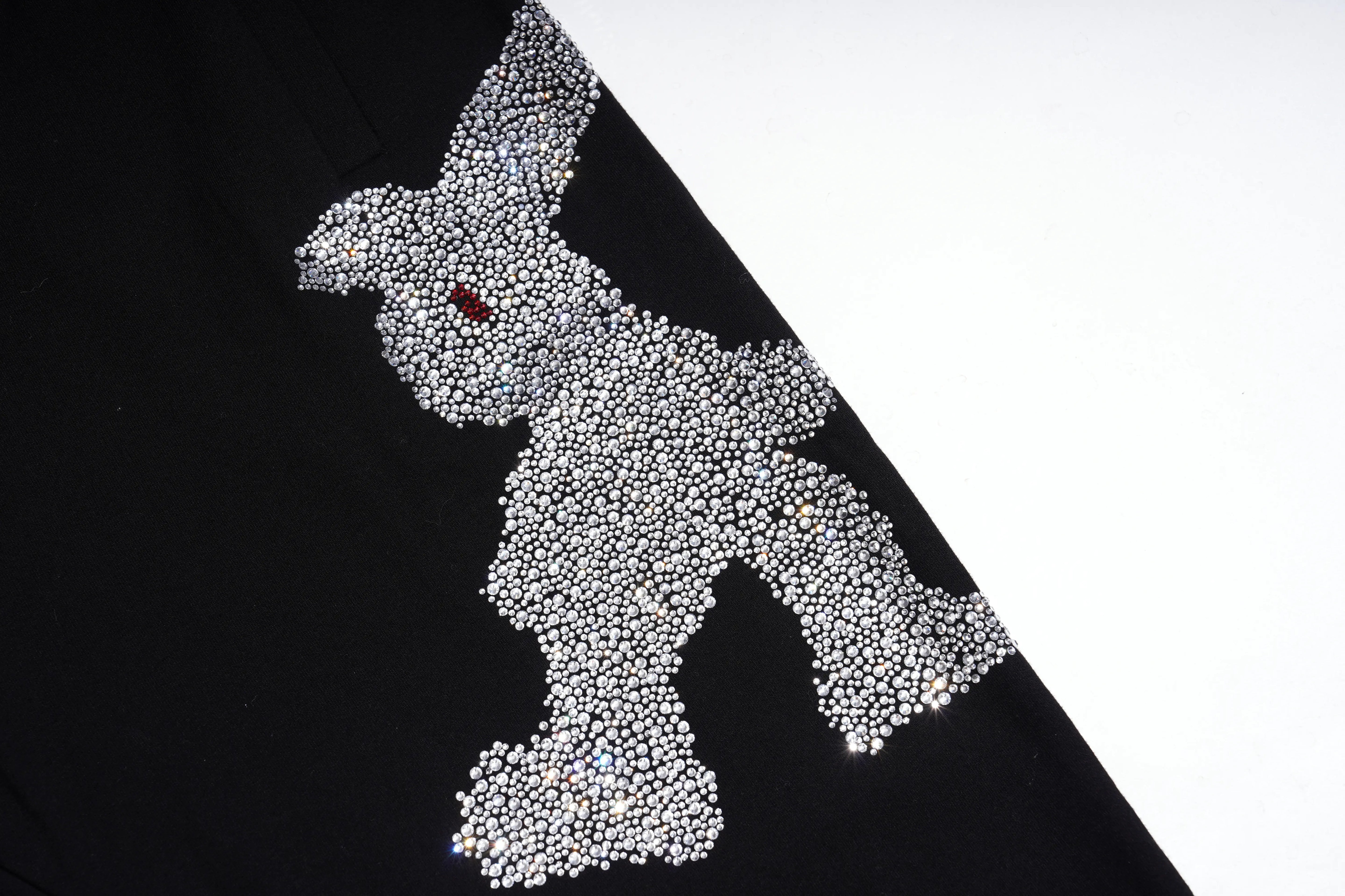 A close-up of a black garment featuring a large rabbit silhouette embellished with thousands of small silver rhinestones, with a tiny red accent at the ear. TCH Rhinestone Teddy Bear Graphic Black Jogger Pants
