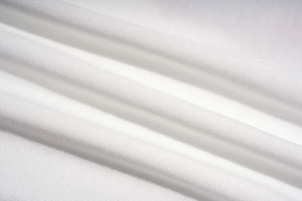 A close-up of draped white fabric with soft folds and a fine woven texture. TCH Rhinestone Teddy Bear Graphic Striped Sleeve Long Sleeve Top