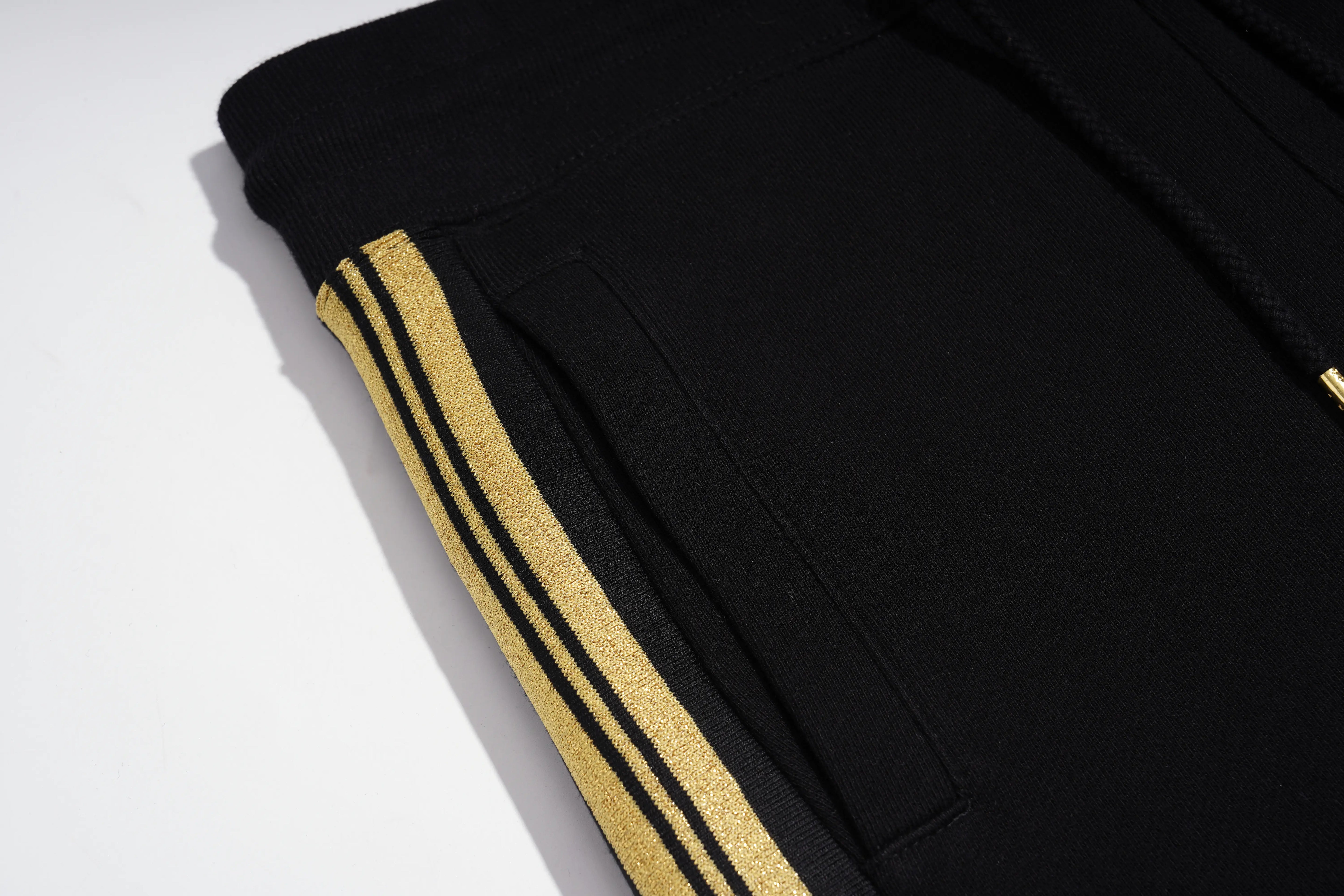 Close-up of black sweatpants with three parallel gold glitter stripes along the side pocket seam, on a white background. TCH Rhinestone Teddy Bear London Graphic Black Jogger Pants