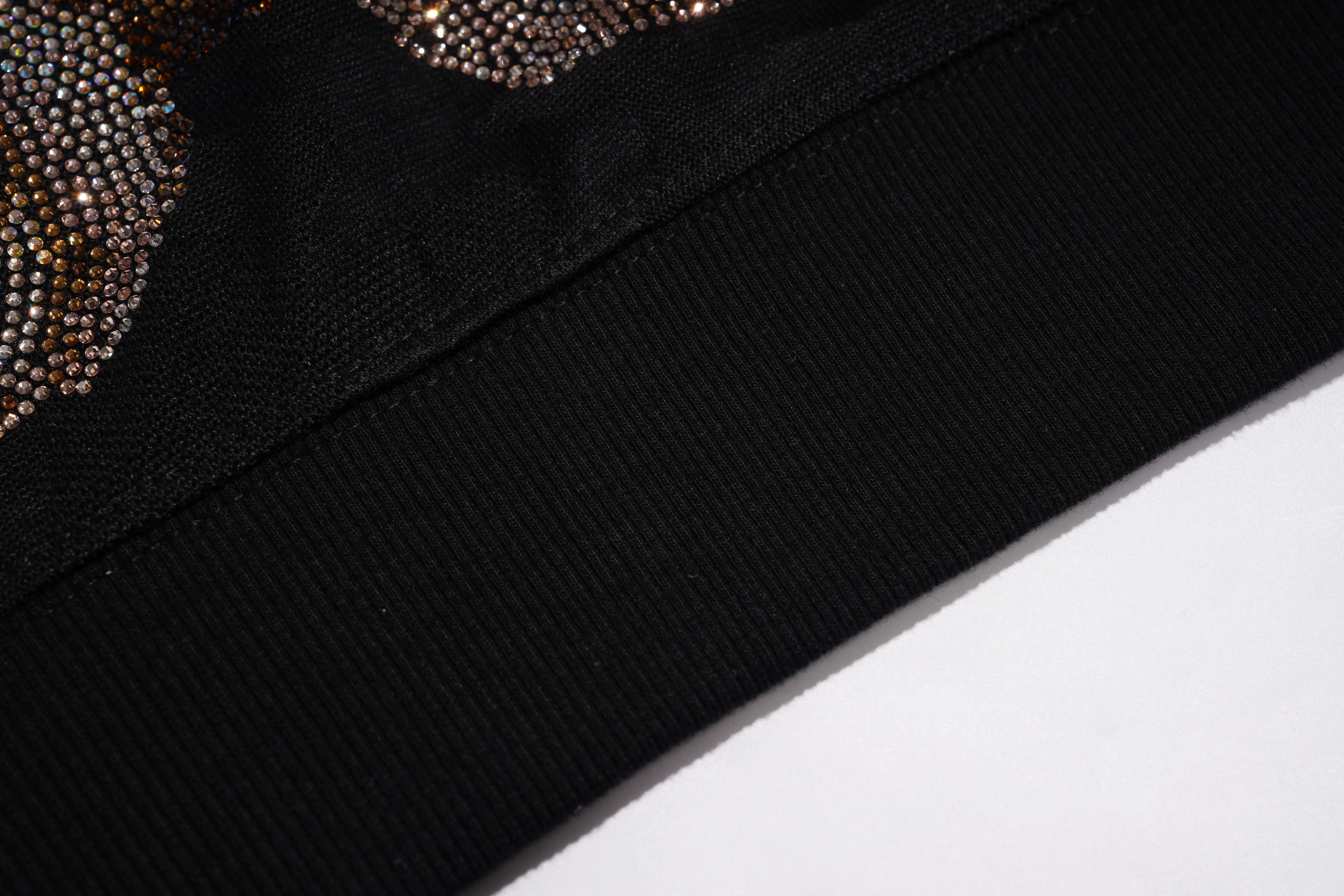 Close-up detail of a black ribbed knit garment, showing a wide ribbed hem and a section of embellished fabric with small metallic rhinestones. TCH Rhinestone Teddy Bear Pearl Chain Graphic Sweatshirt