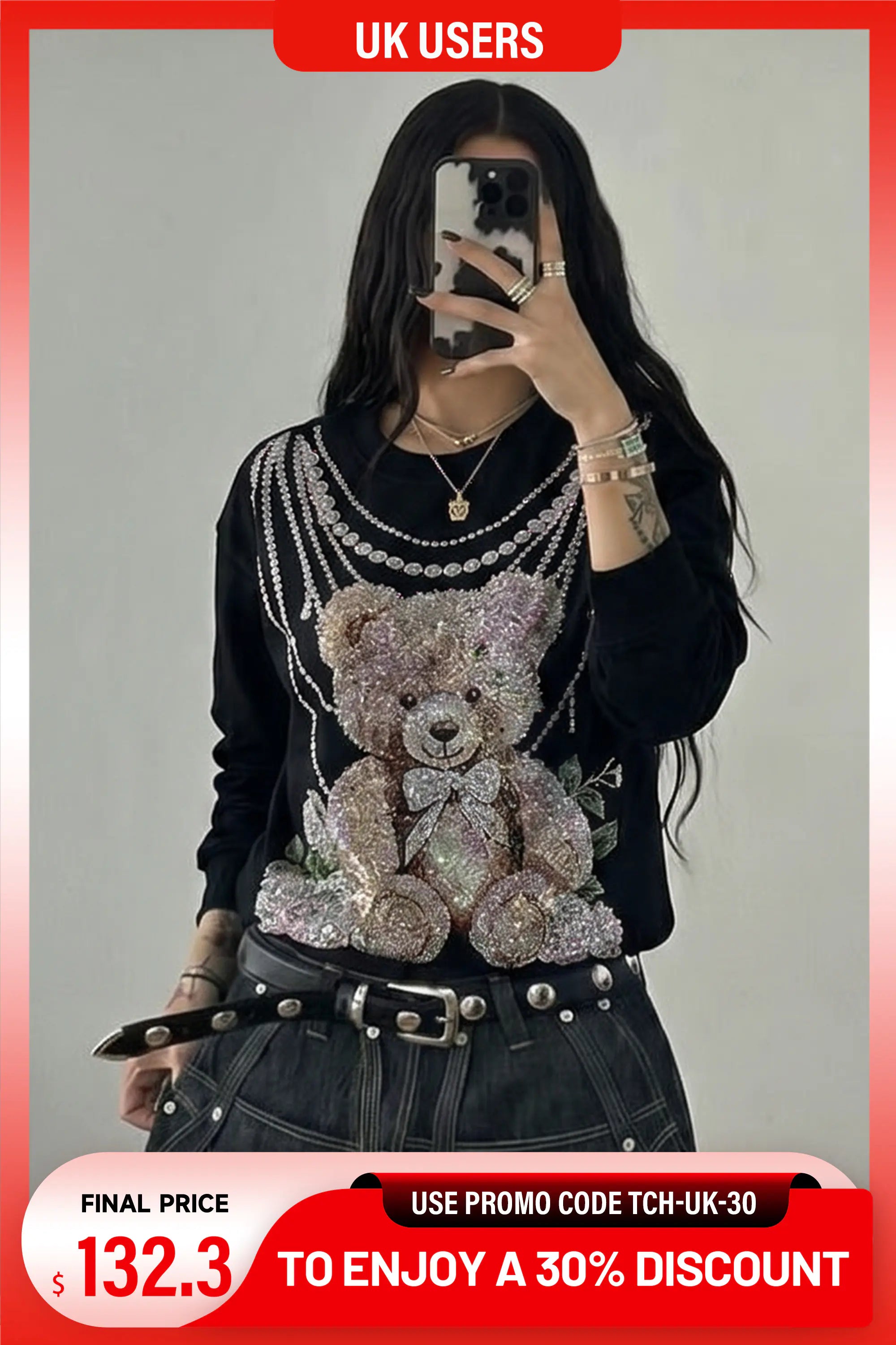 A woman takes a mirror selfie wearing a black long-sleeve top heavily embellished with silver rhinestones and a large teddy bear graphic on the front, paired with dark denim jeans and a studded belt. The image has promotional overlays for UK users showing a final price of $132. TCH Rhinestone Teddy Bear Pearl Chain Graphic Sweatshirt