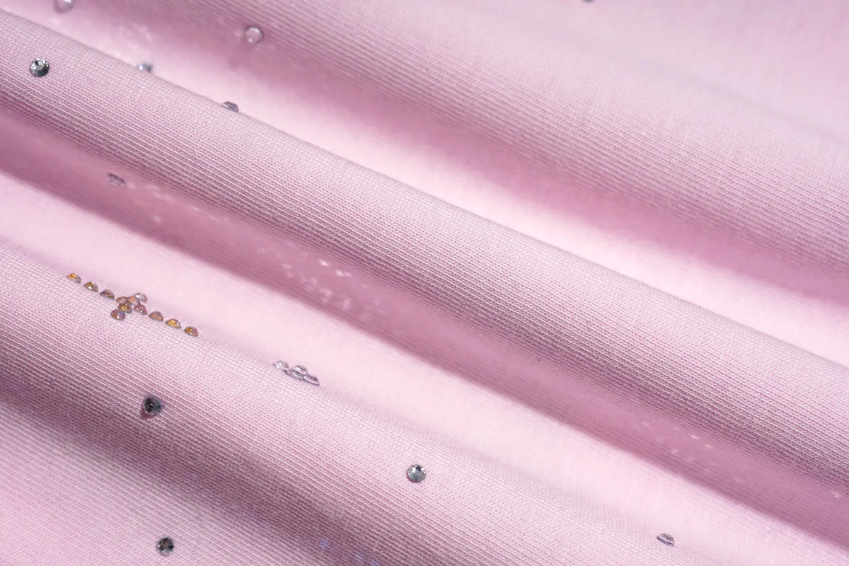 A close-up of light pink ribbed fabric with scattered small rhinestones and a few tiny gold embellishments, arranged in soft diagonal folds. TCH Rhinestone Teddy Bear Pink Long Sleeve T-Shirt