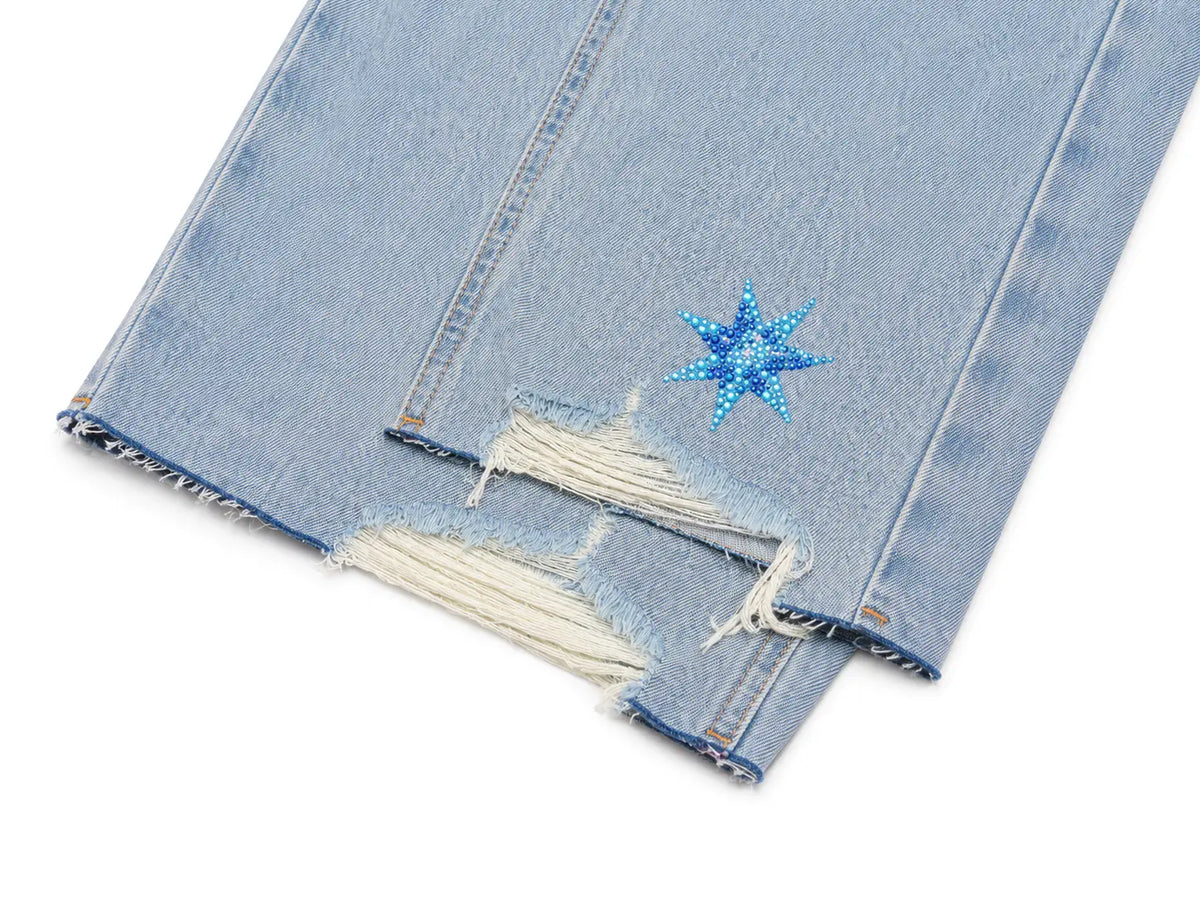 Close-up of light blue distressed denim jeans with a ripped hem and a blue star-shaped embellishment near the pocket, shown on a white background. TCH Rhinestone Teddy Bear Star Wide-Leg Jeans