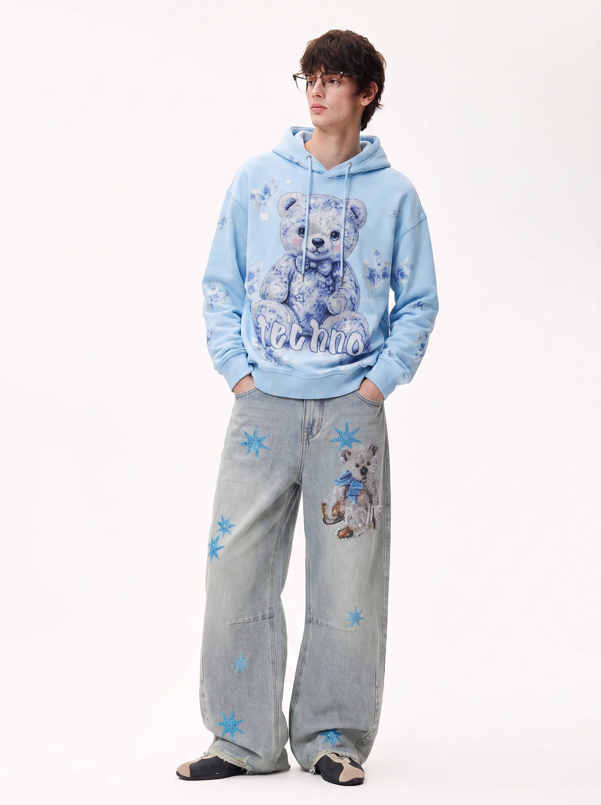 A model wearing a light blue hoodie with a teddy bear graphic and the word 'Mellow' on the front, paired with wide-leg light blue jeans featuring star and bear prints, against a plain white studio background. TCH Rhinestone Teddy Bear Star Wide-Leg Jeans