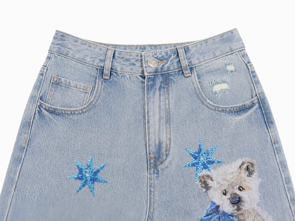 Light blue denim jeans featuring a distressed front pocket with a ripped detail, a blue glittery star patch, and a beaded embroidered puppy on the lower right leg. TCH Rhinestone Teddy Bear Star Wide-Leg Jeans