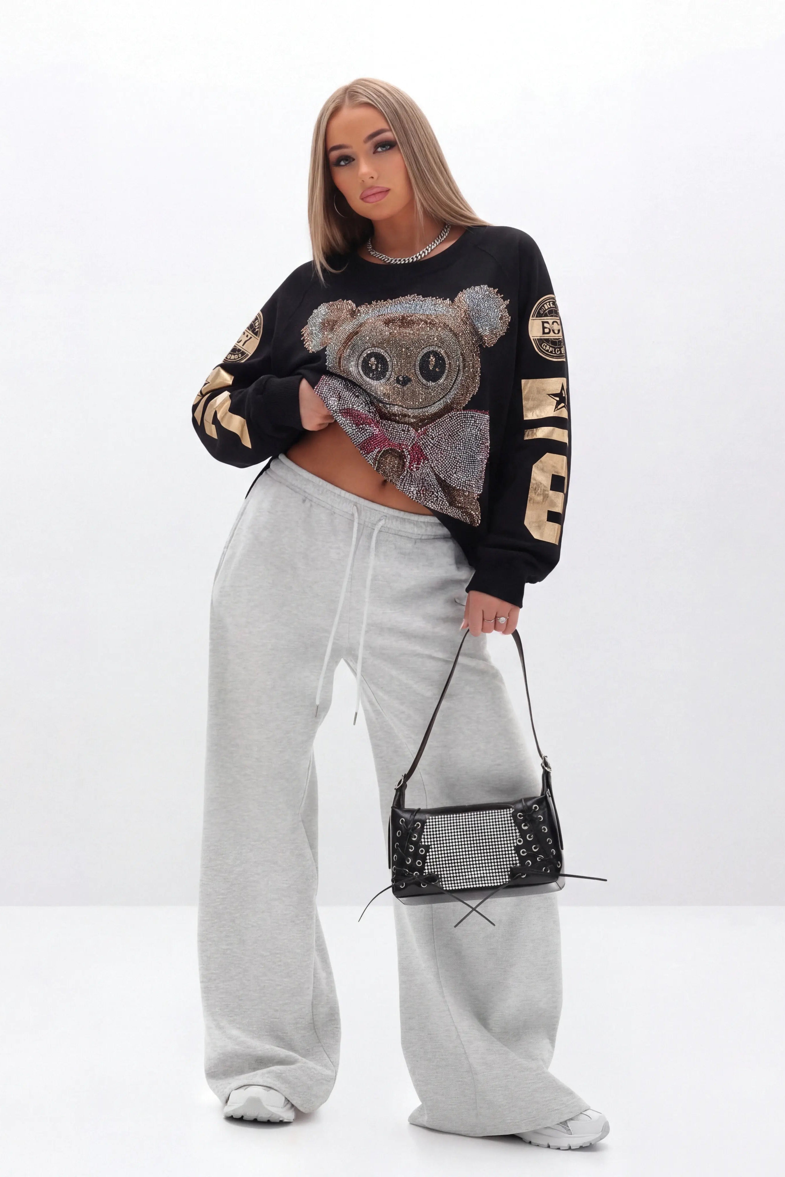 Woman wearing a black sweater with a bear design and gray sweatpants on a white background, TCH Rhinestone Teddy Bear Sweatshirt