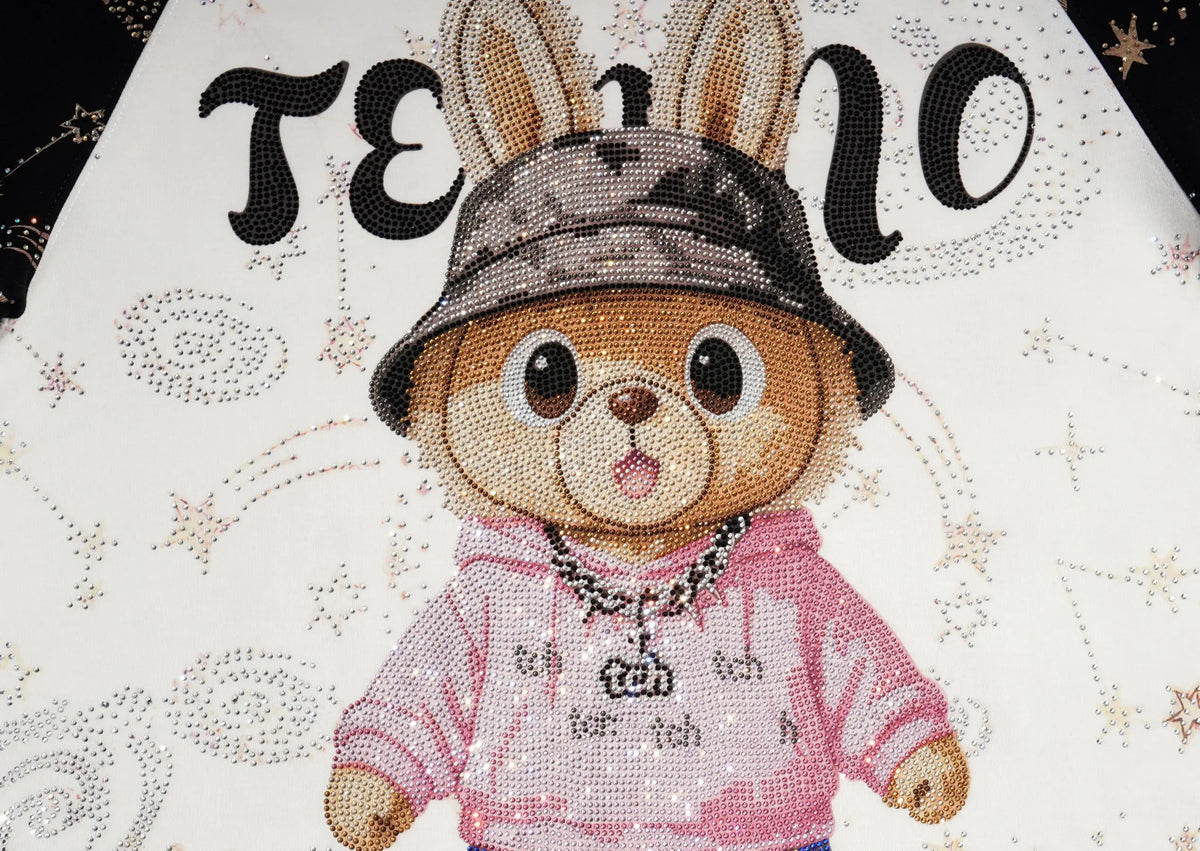 A close-up of a diamond painting or bead art design featuring a cartoon rabbit character wearing a pink hoodie and a dark bucket hat, with the word 'TEEN' in large black letters above on a white background decorated with stars and swirls. TCH Rhinestone Teddy Bear Techno Raglan T-Shirt