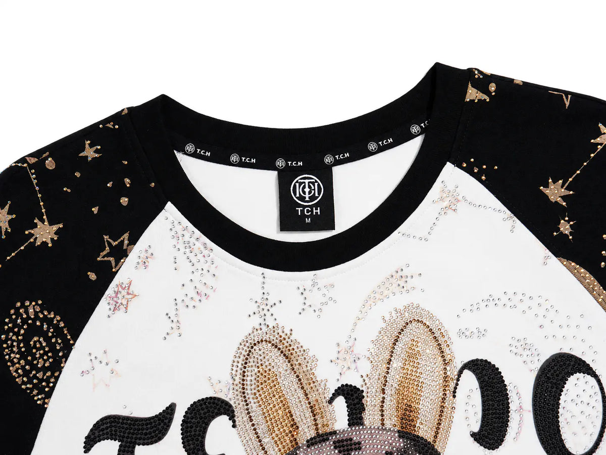 Close-up of a TCH M raglan sweatshirt featuring a white body with black sleeves, embellished with gold rhinestones and star patterns, and a black neck label. TCH Rhinestone Teddy Bear Techno Raglan T-Shirt