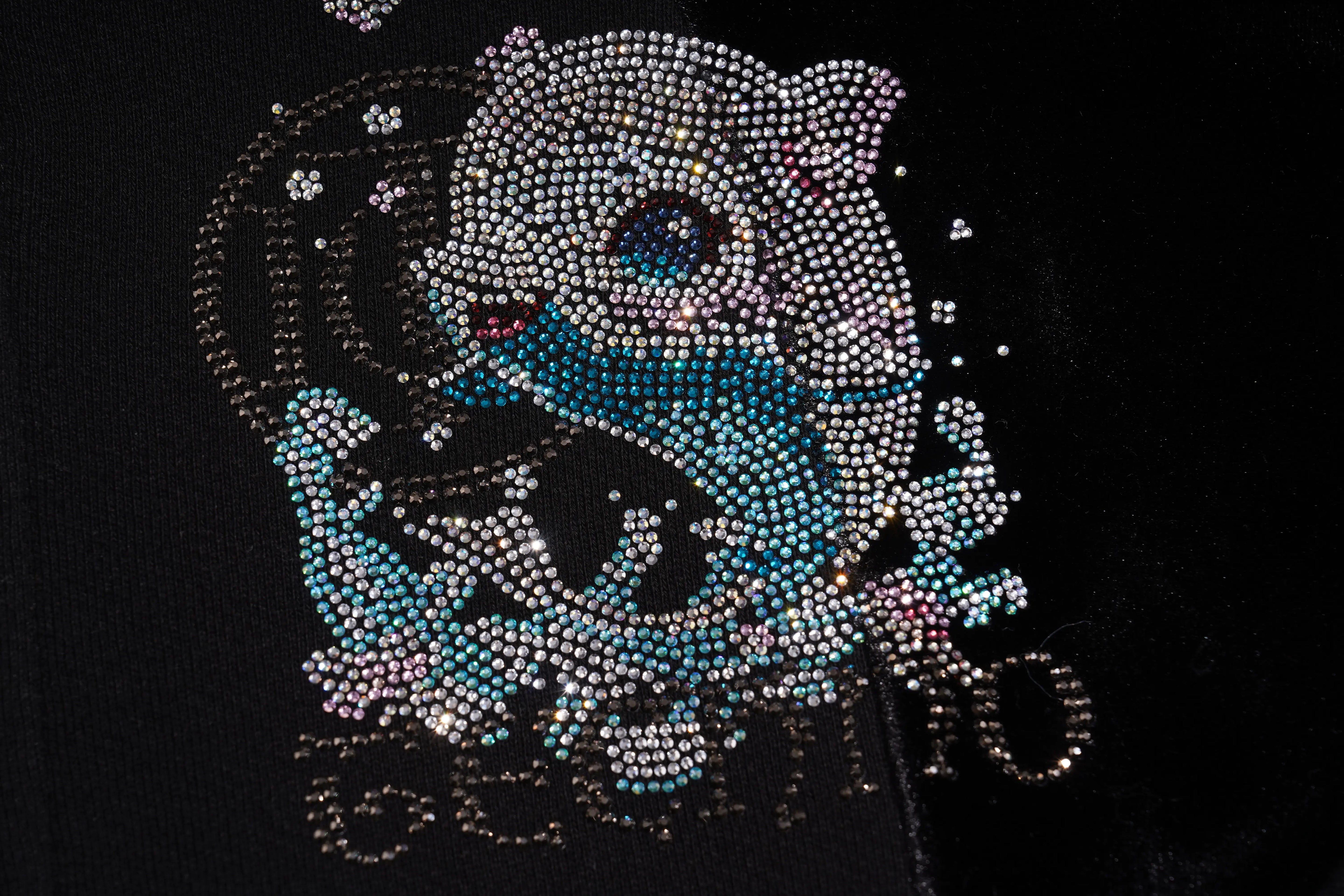 A close-up of a black garment featuring a large, ornate rhinestone graphic of a cat in shades of silver, blue, and pink, with the word 'SEMPER' in matching rhinestones below. TCH Rhinestone Teddy Bear Wing Sleeve Bomber Jacket