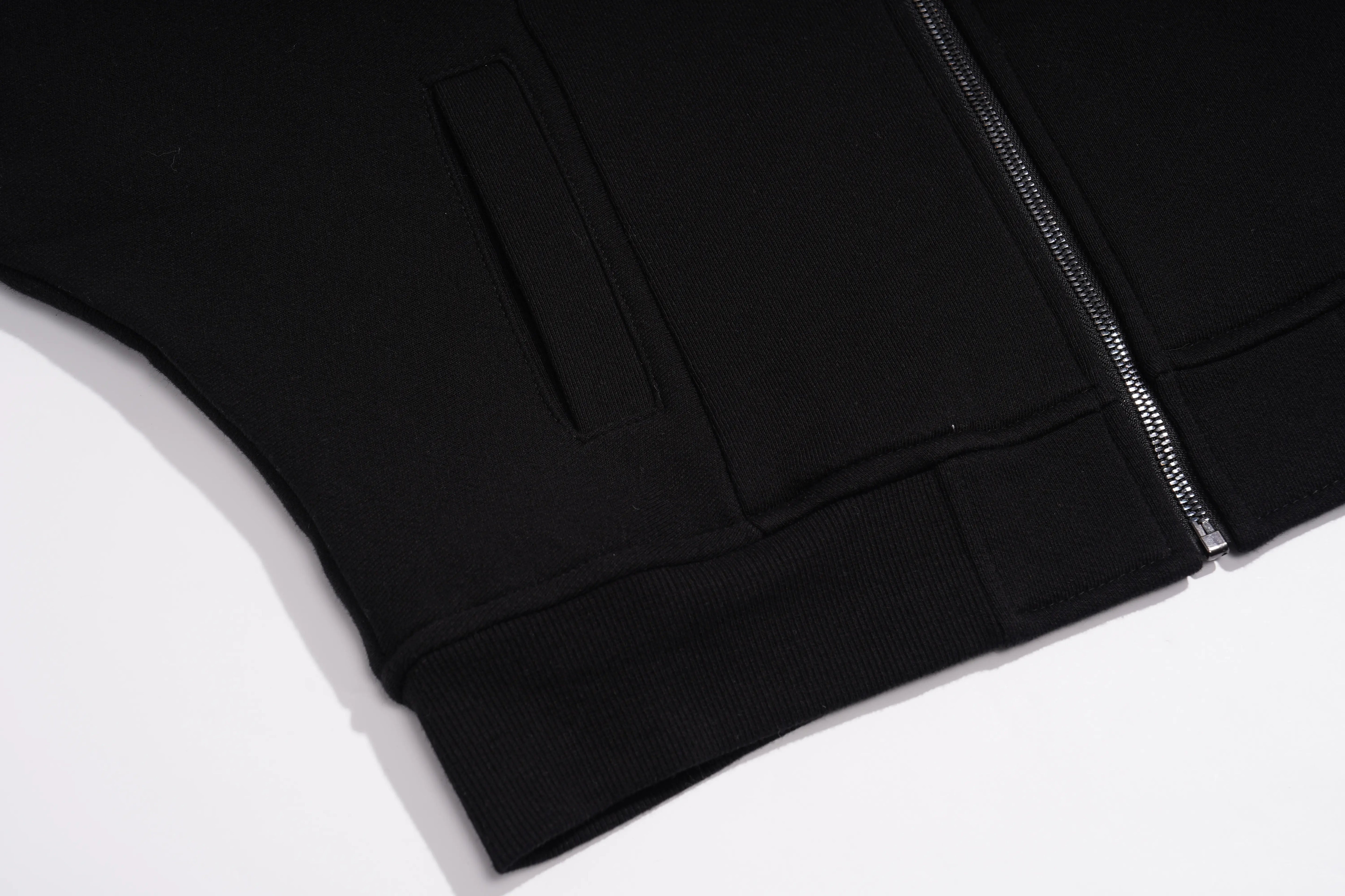 Close-up of a black zip-up jacket or sweatshirt showing the ribbed hem, a side pocket seam, and a silver zipper on a white background. TCH Rhinestone Teddy Bear Wing Sleeve Bomber Jacket