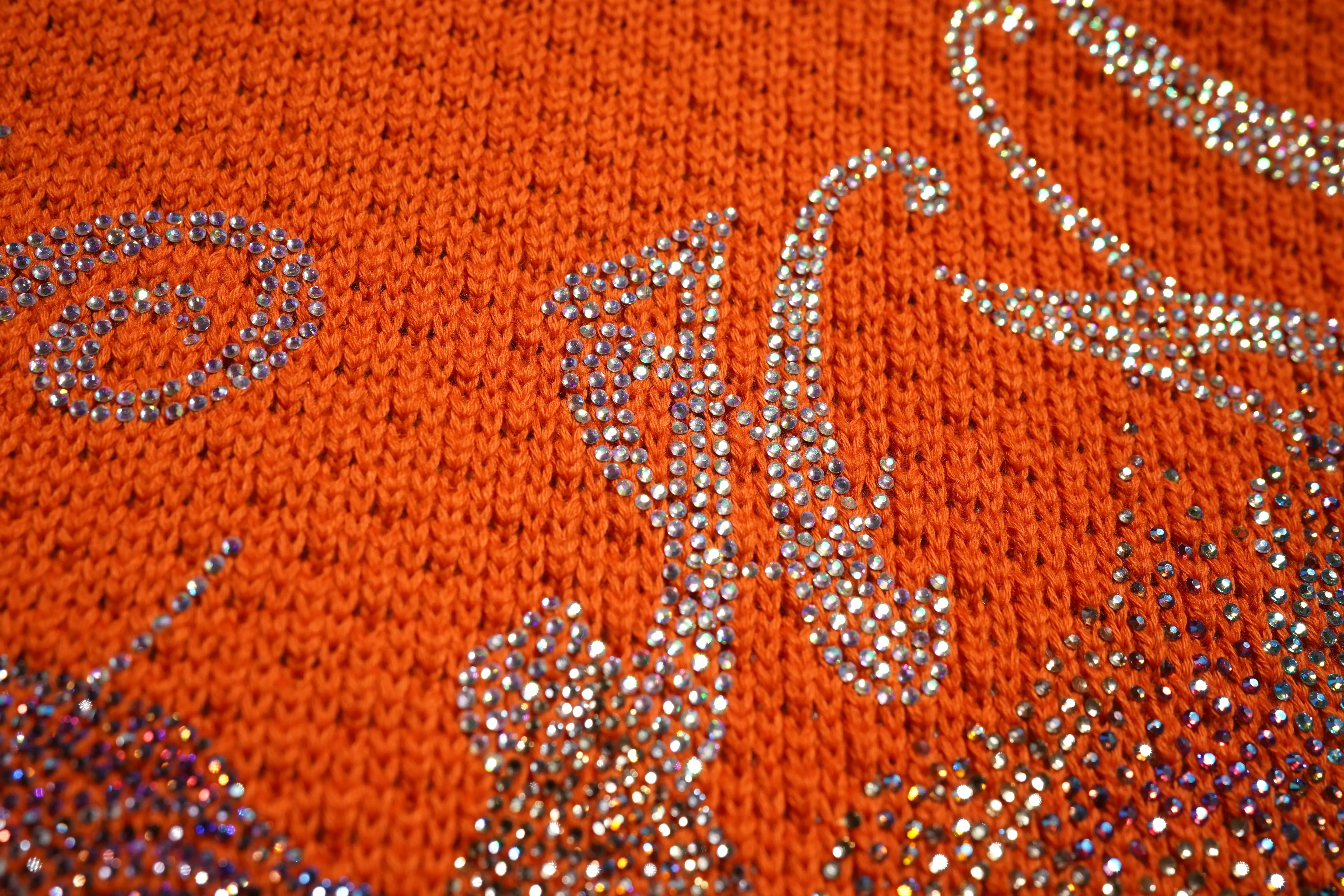 Close-up of a textured orange fabric with decorative patterns and embellishments. TCH Rhinestone Unicorn Orange Hoodie