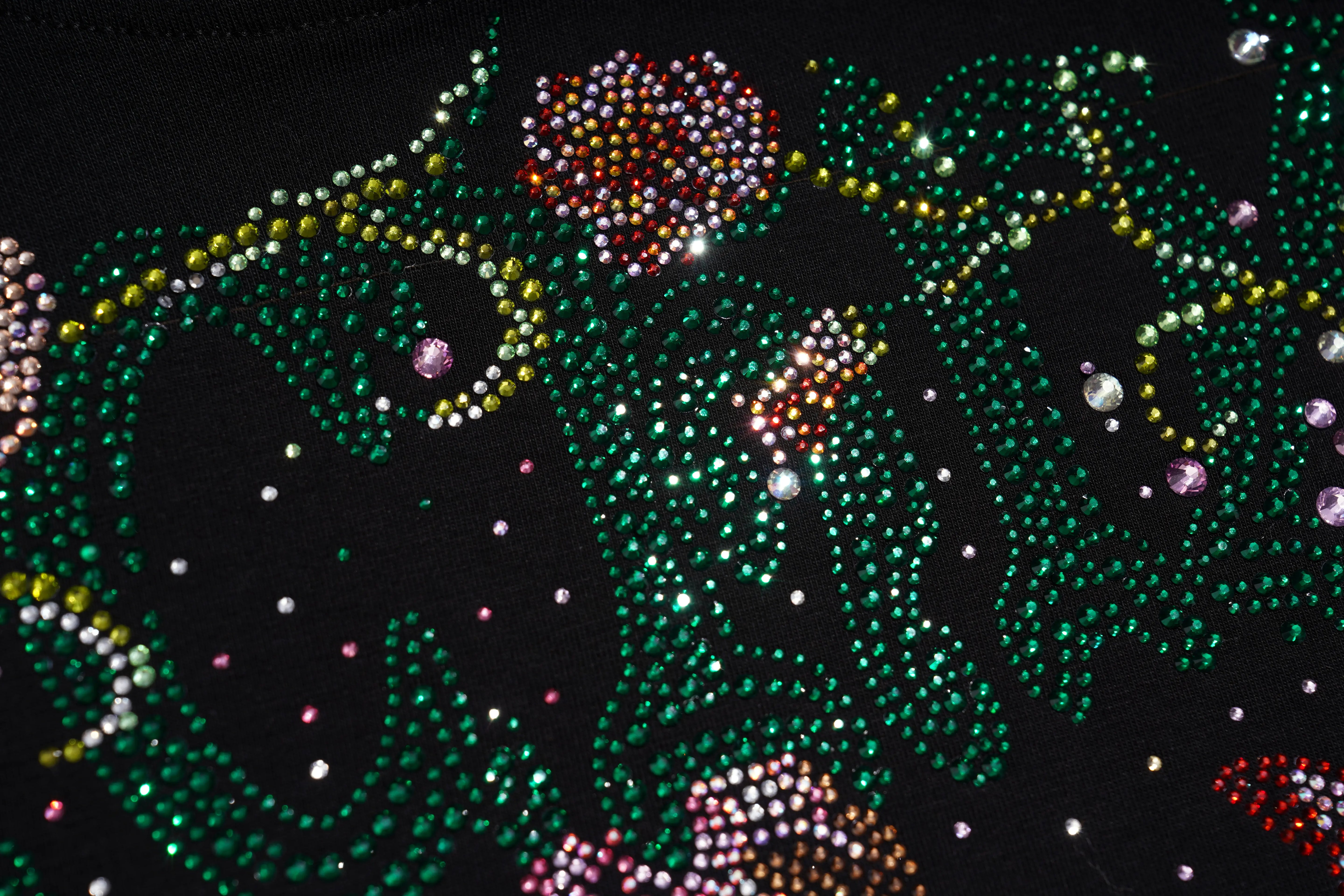 Close-up of a black garment covered with dense rhinestone embellishment in green, gold, pink, and silver, forming an abstract floral or decorative pattern. TCH Rhinestone Vintage Floral Artwork Graphic Black T-Shirt