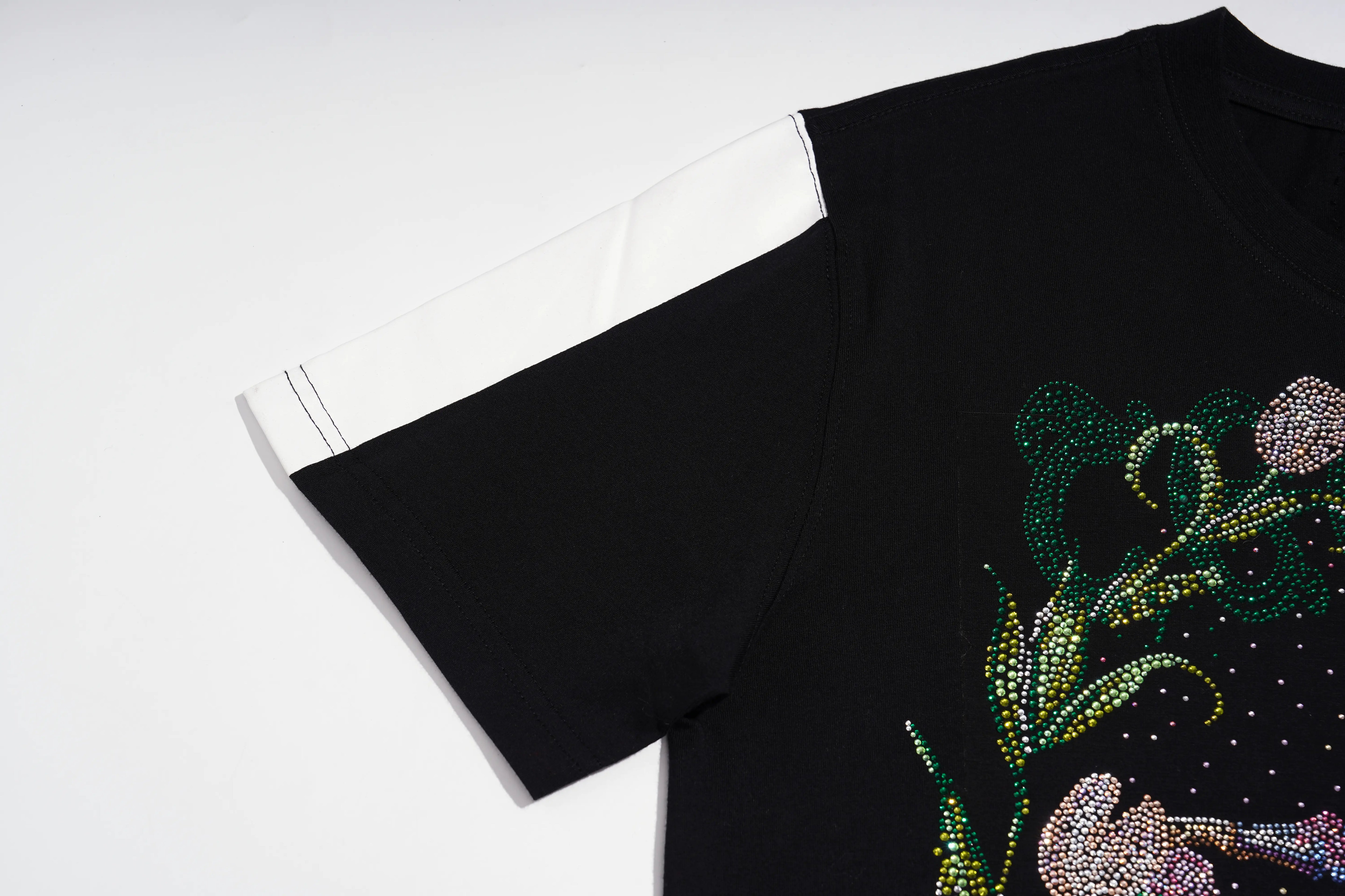 Close-up of a black short-sleeve T-shirt laid flat on a white background, featuring a white contrast panel on the upper sleeve and a rhinestone-embellished floral graphic on the front. TCH Rhinestone Vintage Floral Artwork Graphic Black T-Shirt