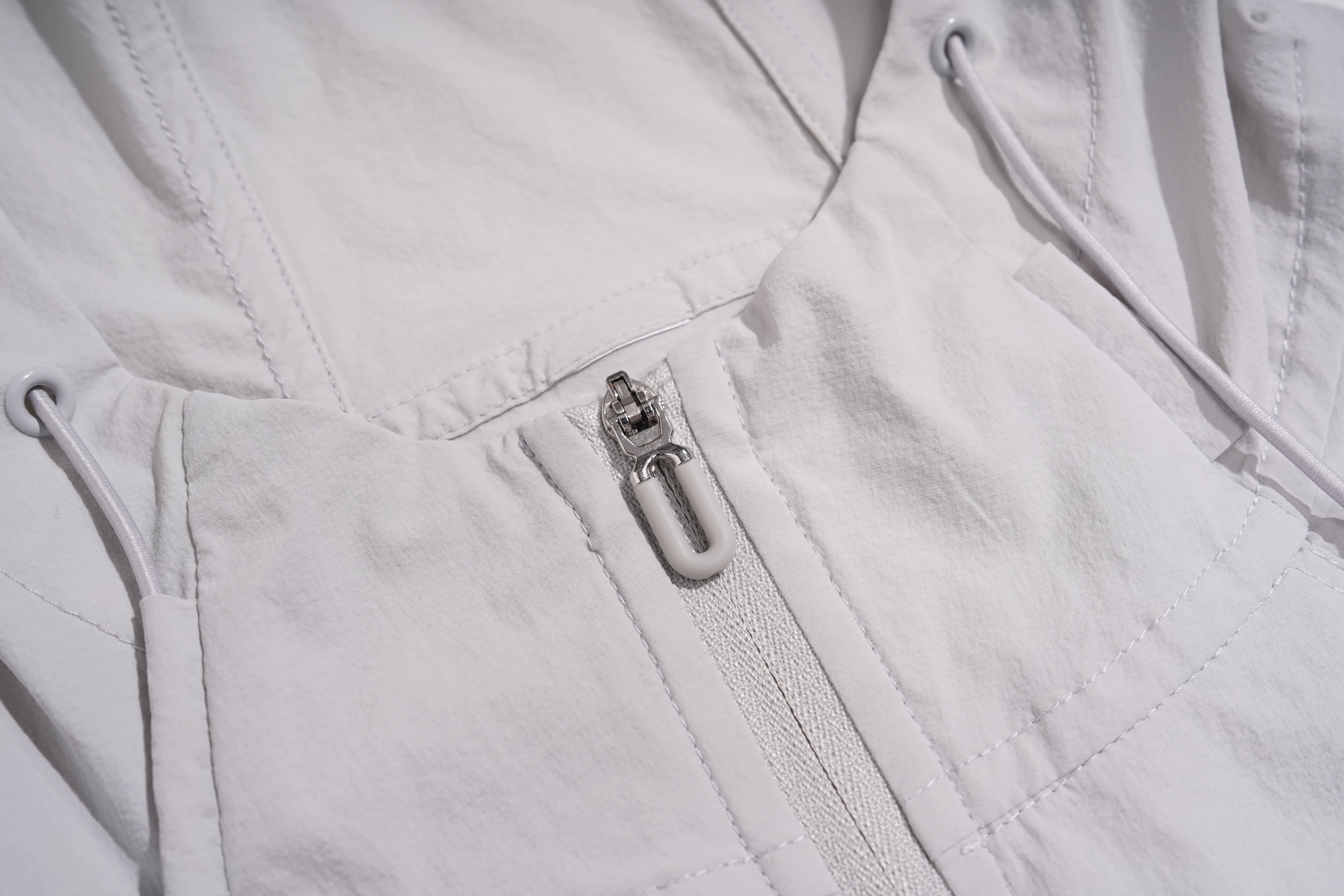 Close-up detail of a white lightweight zippered garment, showing the silver metal zipper pull and stitched paneling. TCH Rhinestone Wing Active 3-Piece Tracksuit Set