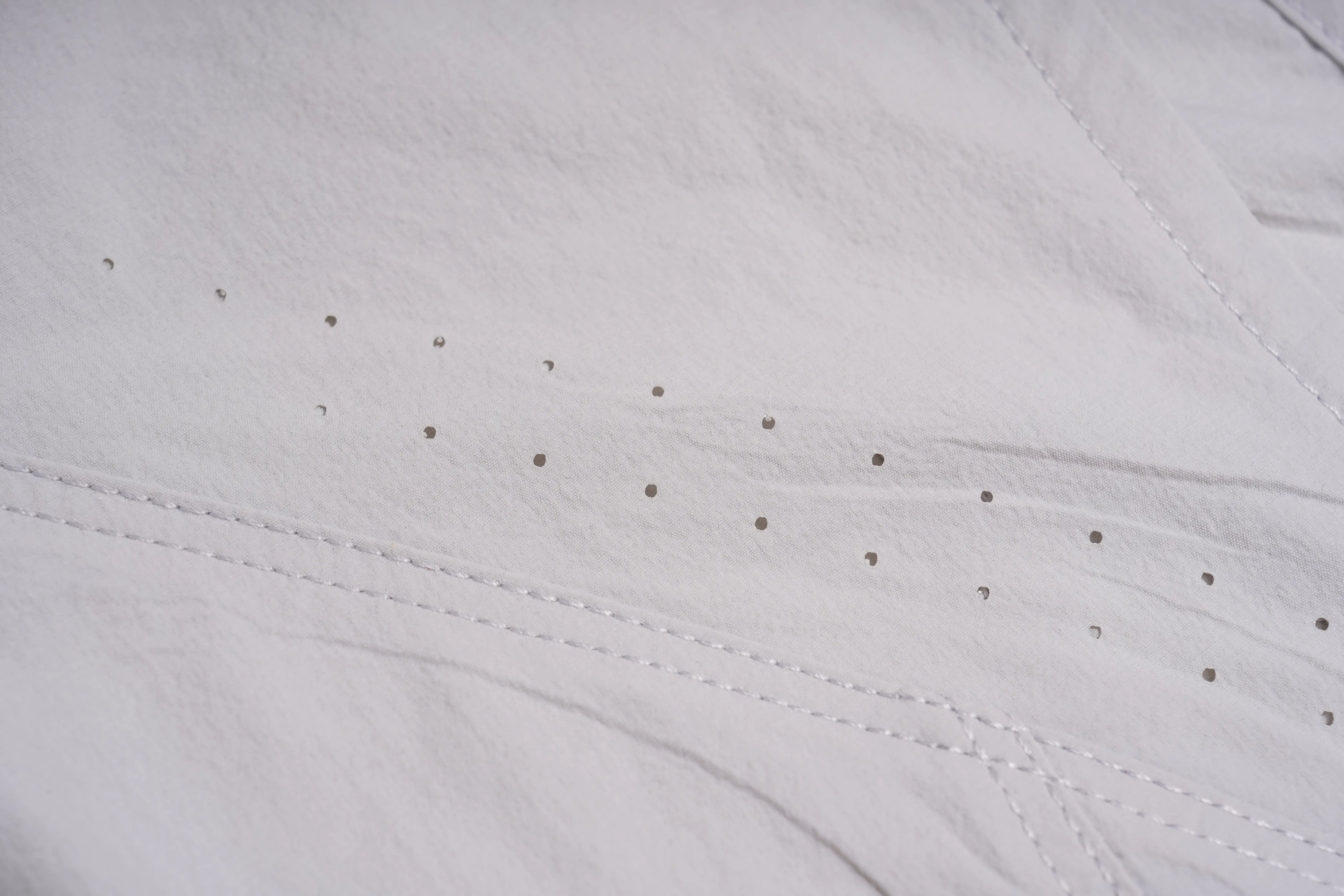 Close-up of a white textured fabric with fine perforations and stitched details. TCH Rhinestone Wing Active 3-Piece Tracksuit Set