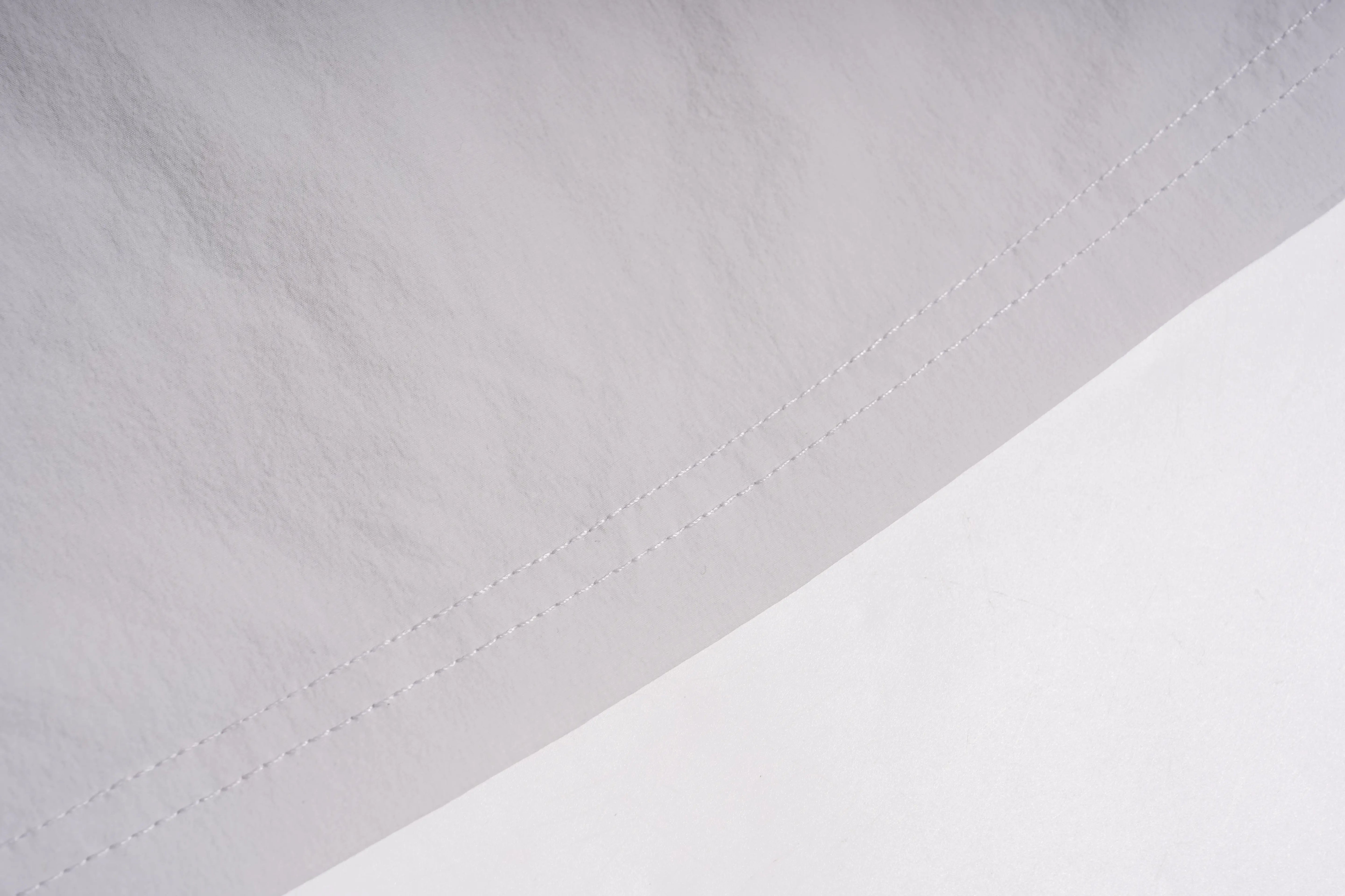 Close-up of a white fabric surface with a diagonal stitched seam and a lighter white area below it. TCH Rhinestone Wing Active 3-Piece Tracksuit Set