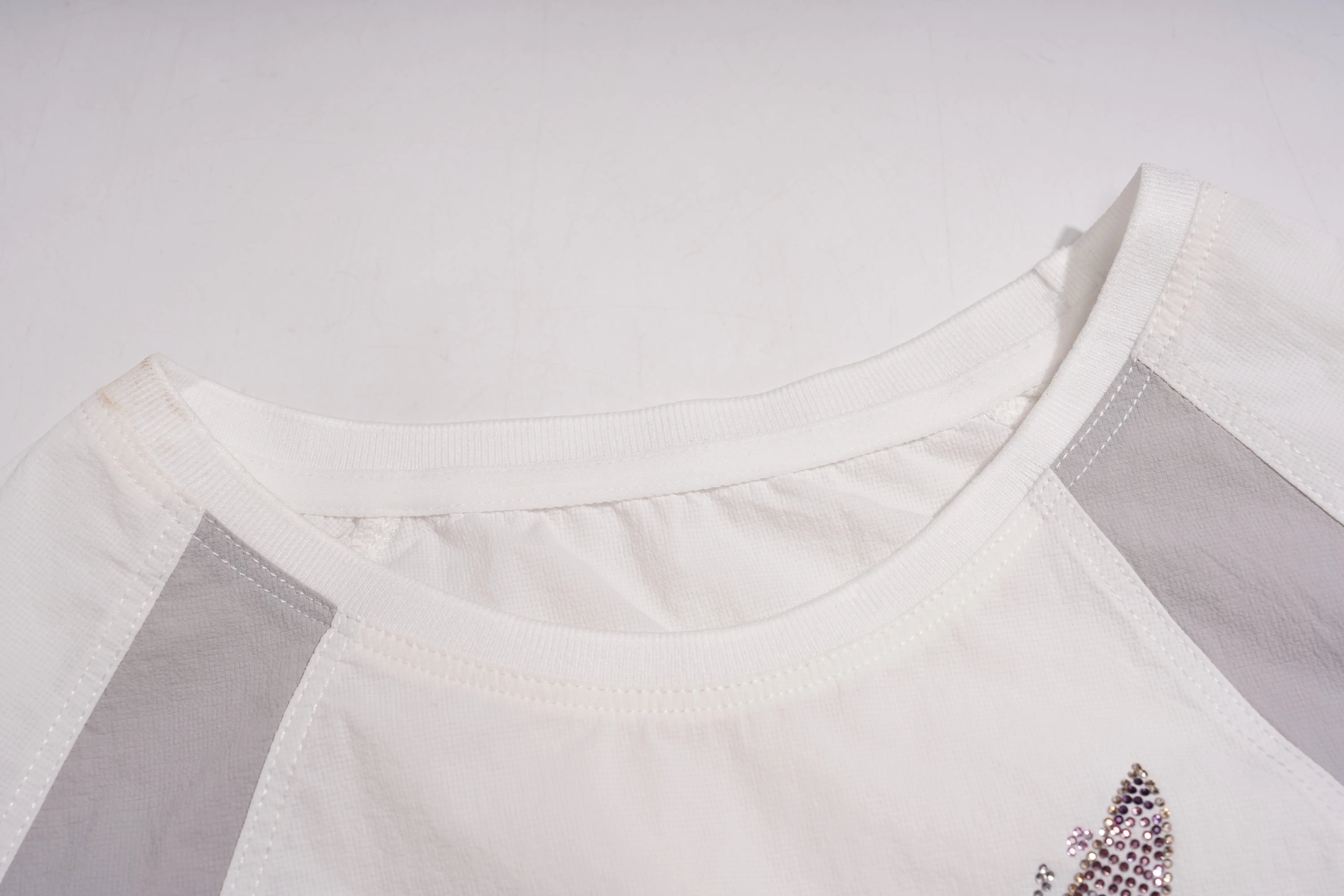 Close-up of a white raglan-style top with light gray side panels and a small sequined embellishment near the lower right side, shown against a plain light background. TCH Rhinestone Wing Active 3-Piece Tracksuit Set