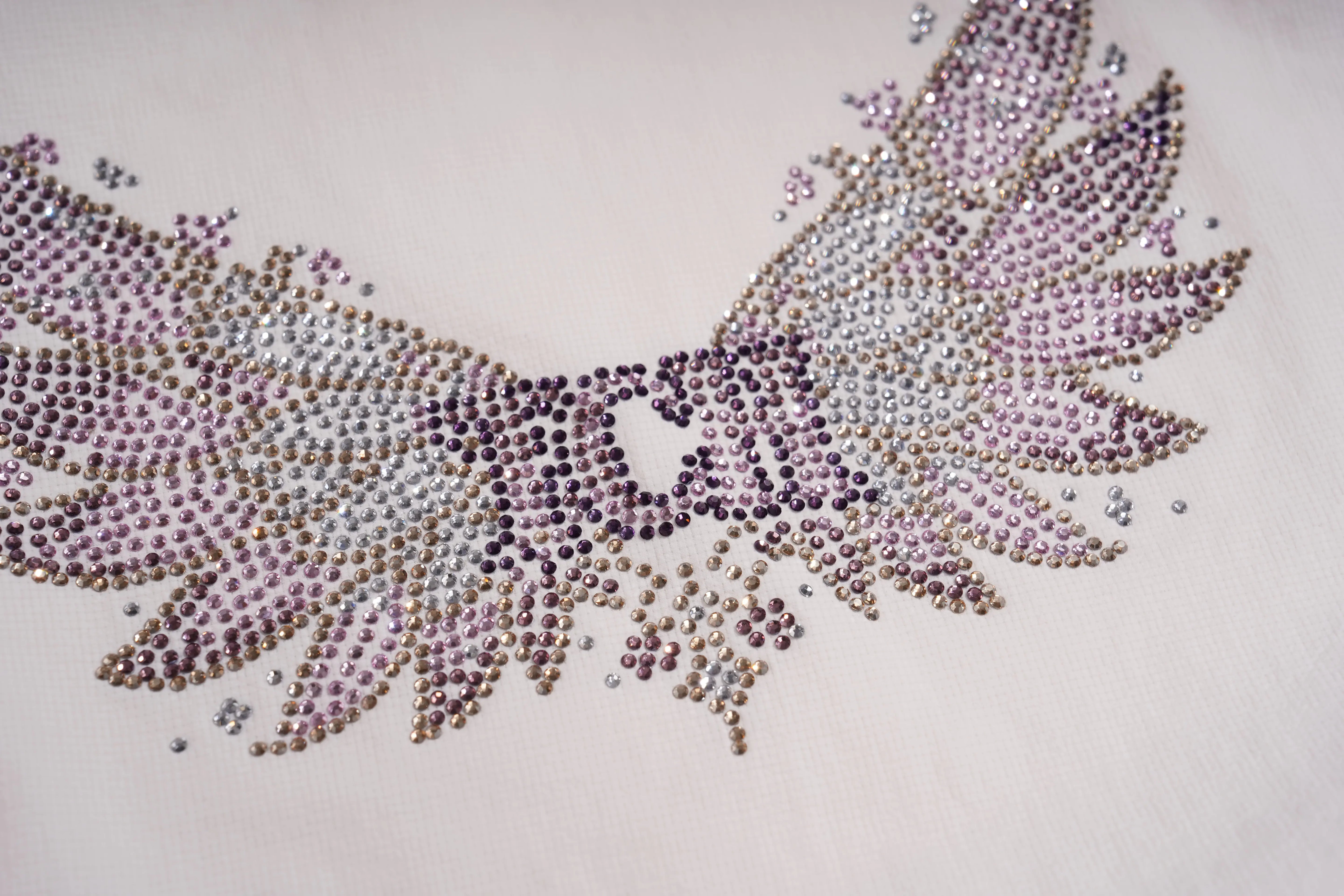 A close-up of a rhinestone-embellished wing motif on a light cream fabric background. The wings are decorated with small, reflective rhinestones in shades of lavender, silver, and dark purple. TCH Rhinestone Wing Active 3-Piece Tracksuit Set