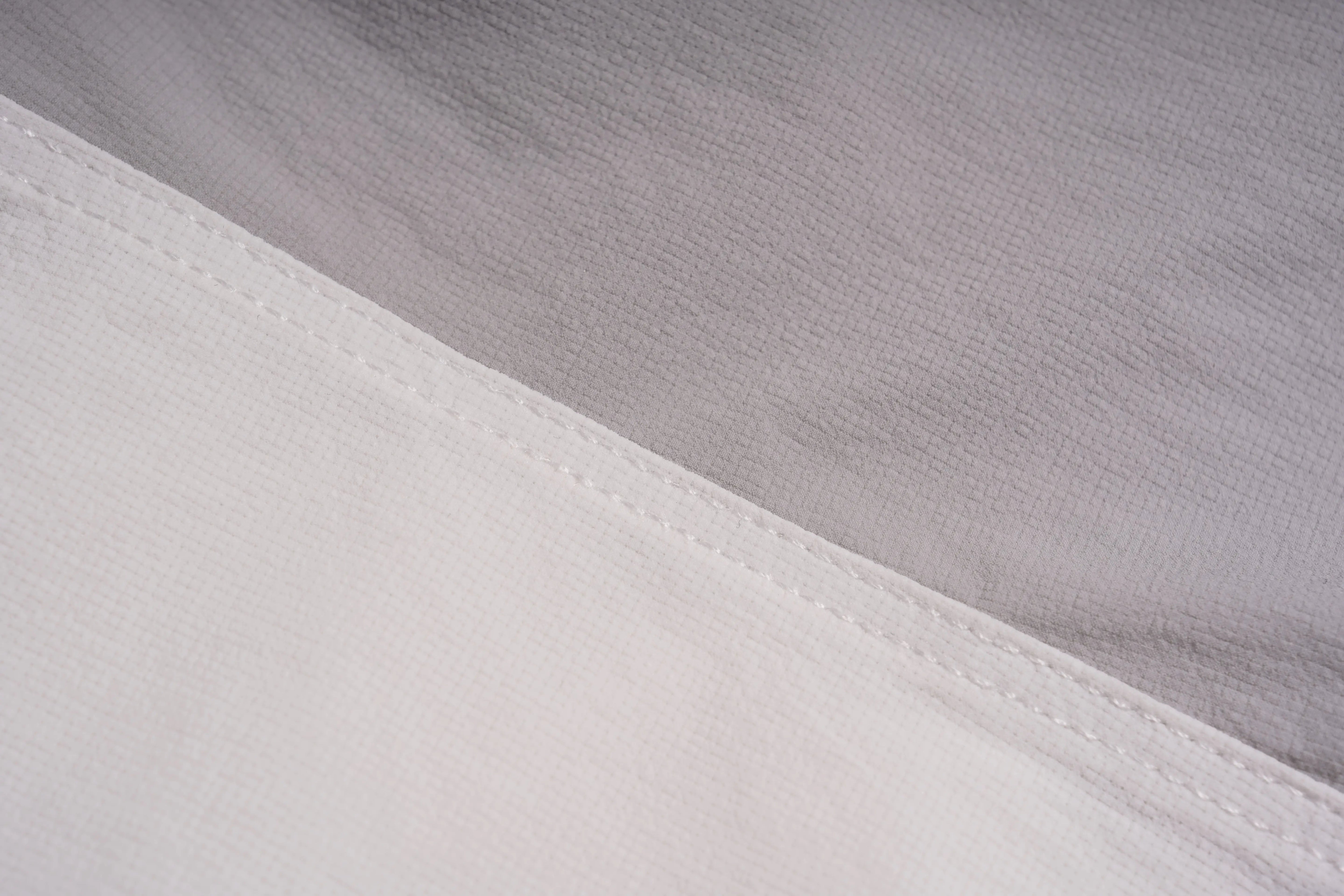 Close-up of a white fabric surface with a diagonal seam and a slightly textured light gray fabric behind it. TCH Rhinestone Wing Active 3-Piece Tracksuit Set