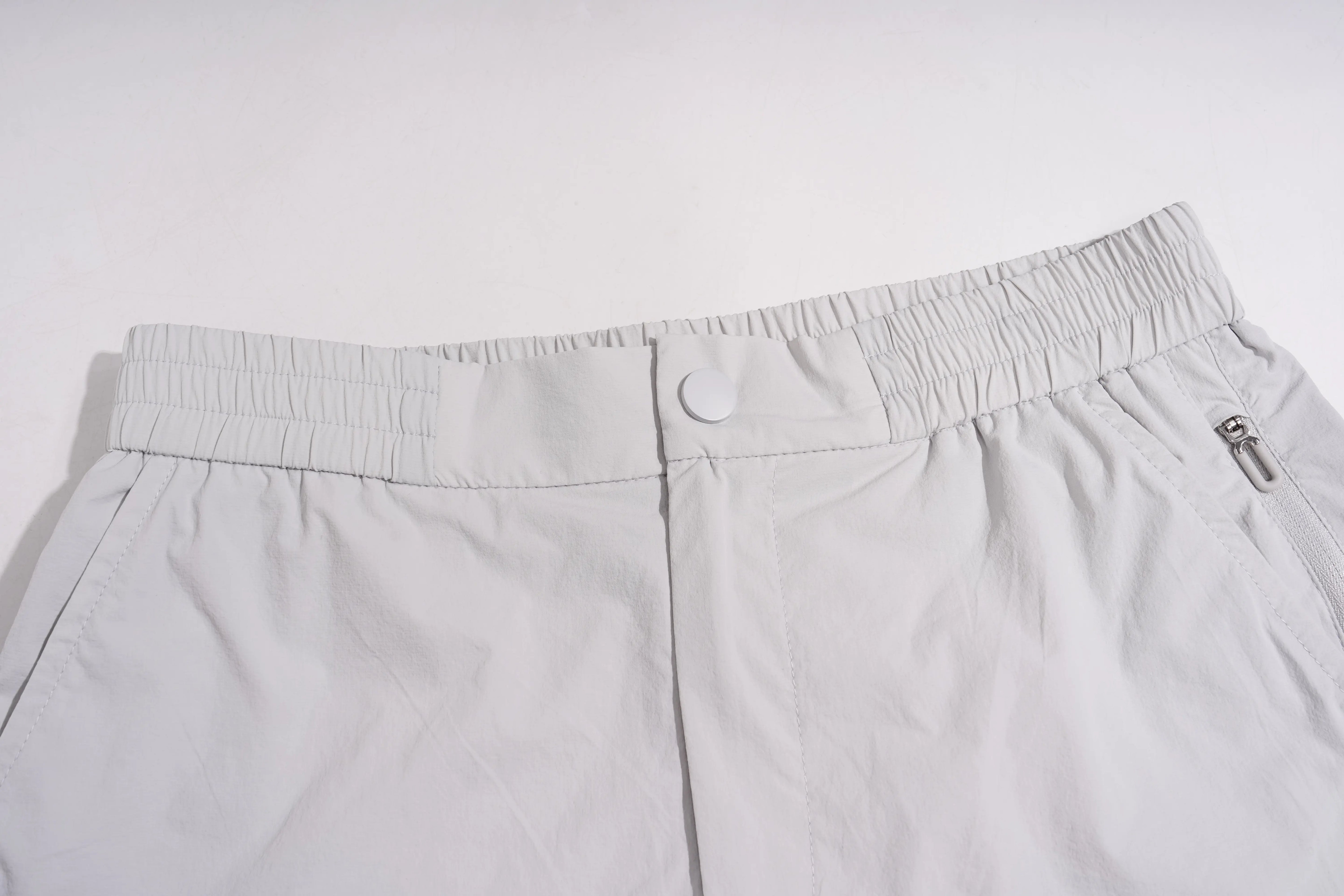 Close-up of a pair of light gray athletic shorts showing the elastic waistband, button closure, and side zip pocket. TCH Rhinestone Wing Active 3-Piece Tracksuit Set