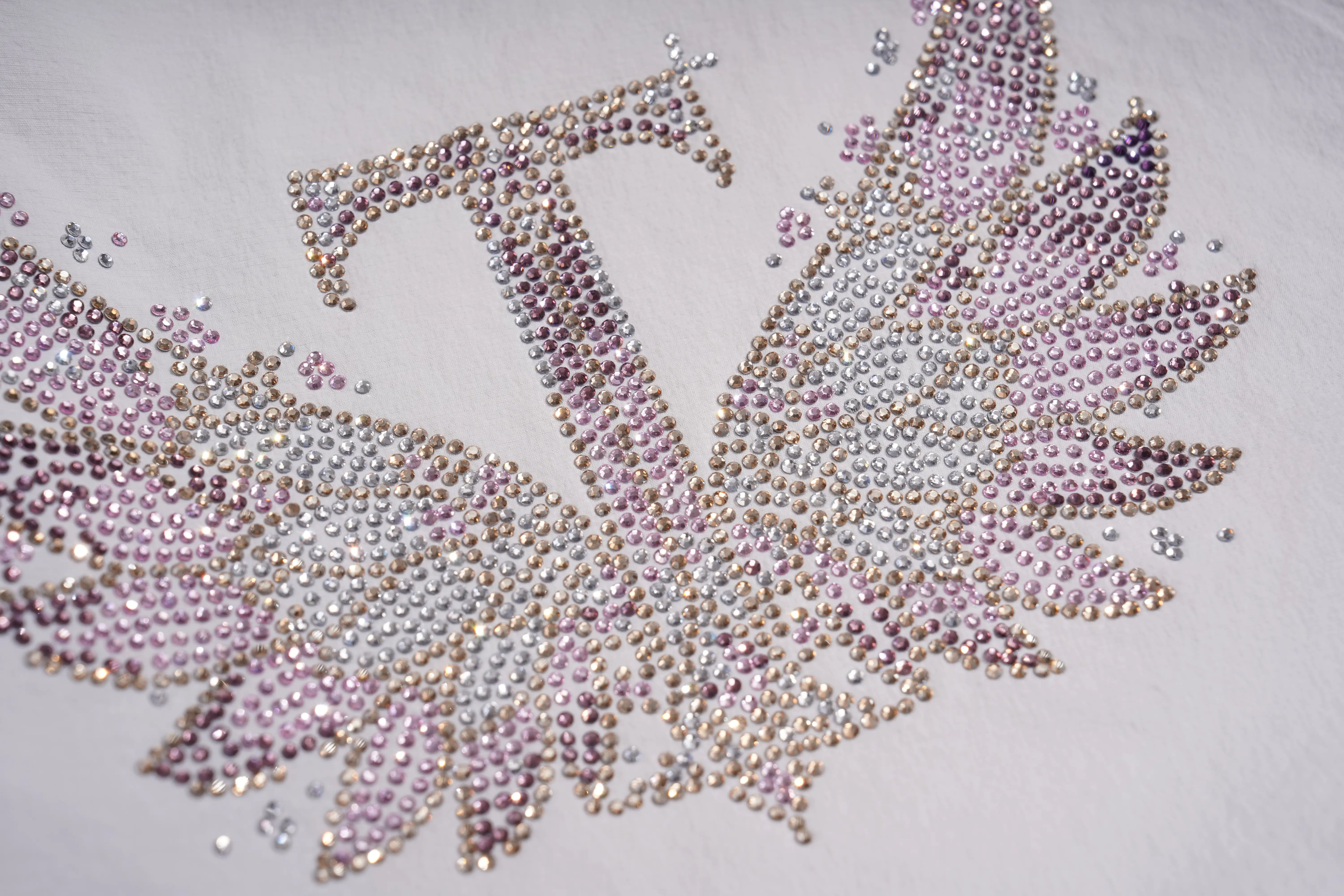 A close-up of a rhinestone-embellished letter T with angel wings, featuring pink, silver, and gold rhinestones on a white fabric background. TCH Rhinestone Wing Active 3-Piece Tracksuit Set