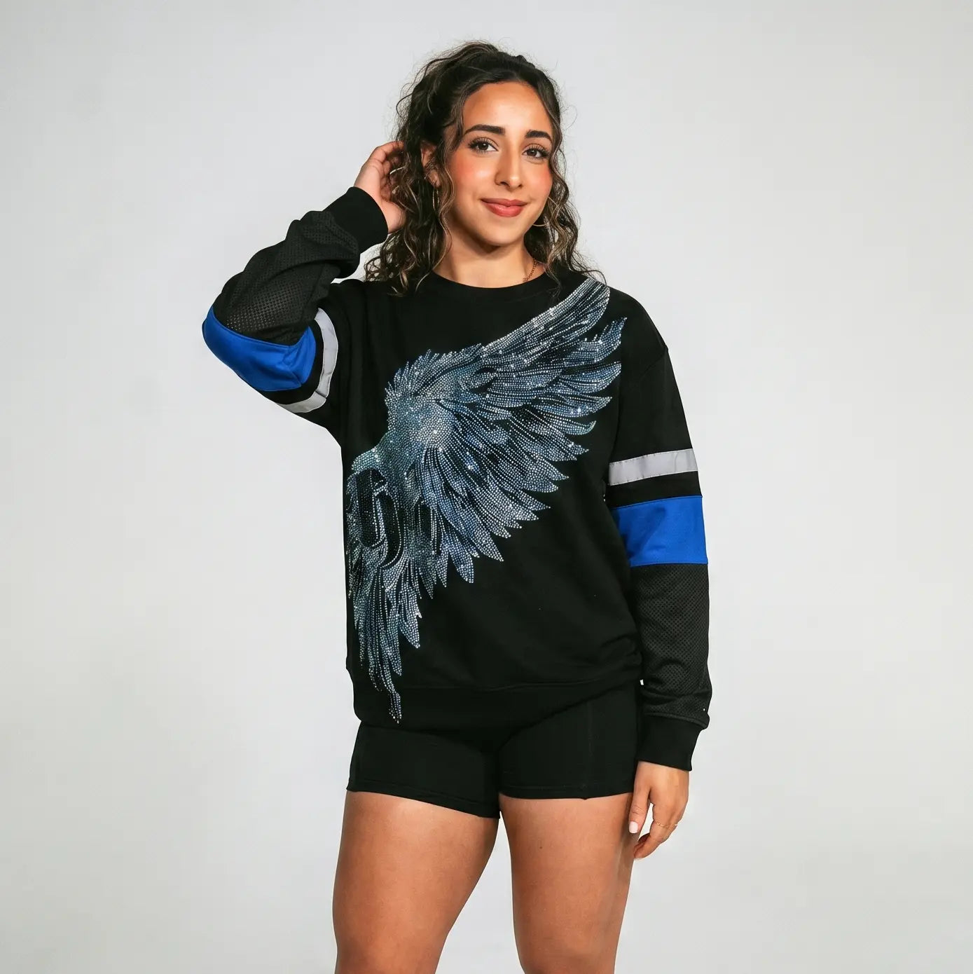 Woman wearing a black sweatshirt with blue sleeves and a large wing design on a plain background, TCH Rhinestone Wing Black Crewneck Sweatshirt