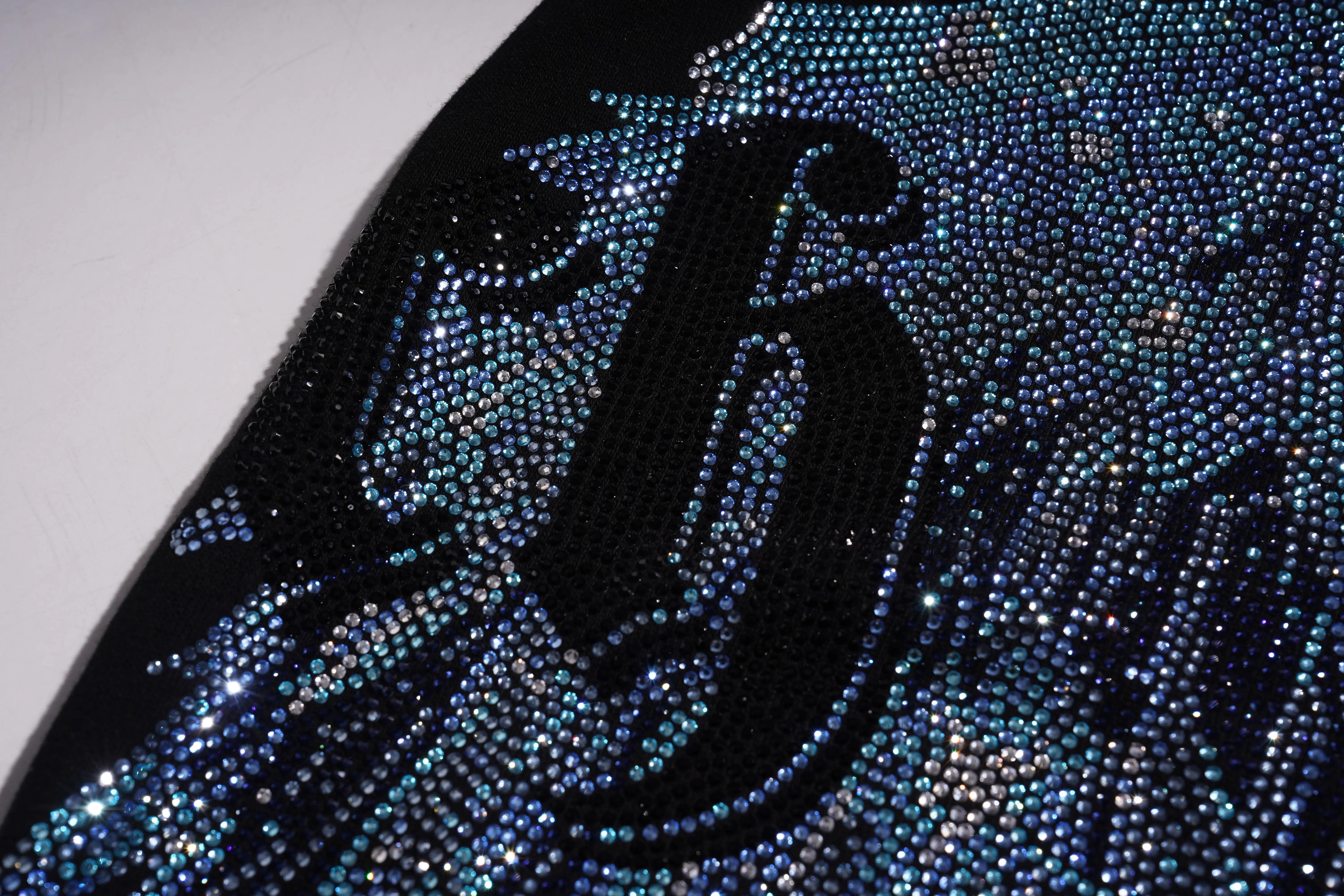 Close-up of a black number '9' on a surface covered with blue rhinestones. TCH Rhinestone Wing Black Crewneck Sweatshirt