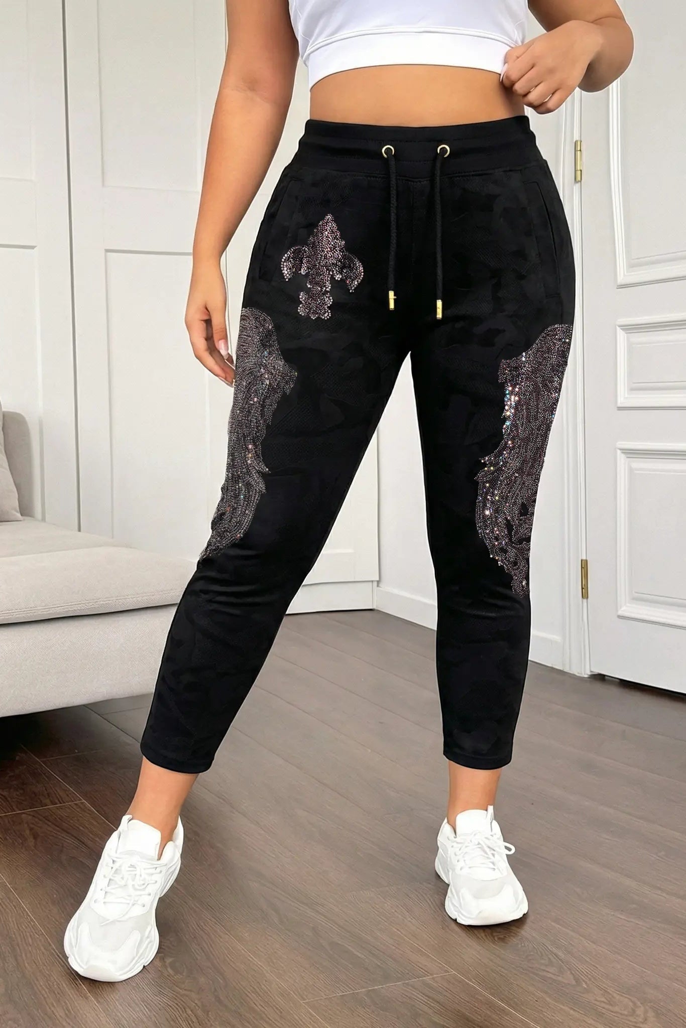 Person wearing black sequin pants in a room with a couch and white walls. TCH Rhinestone Wing Camo Jogger Pants