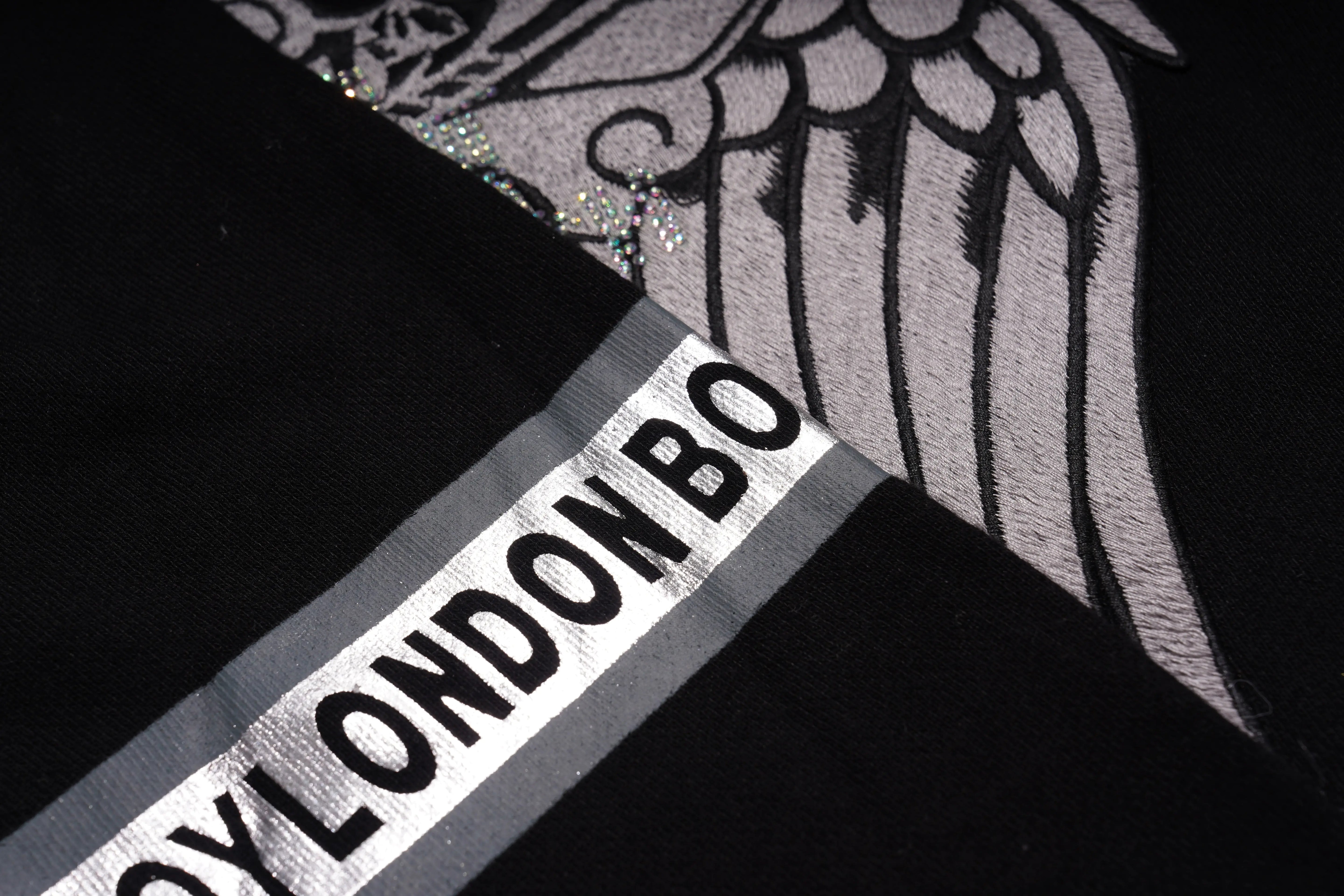 Close-up of a product with 'Dylondon' branding and winged design. TCH Rhinestone Wing Crest Embroidered Sweatshirt-6