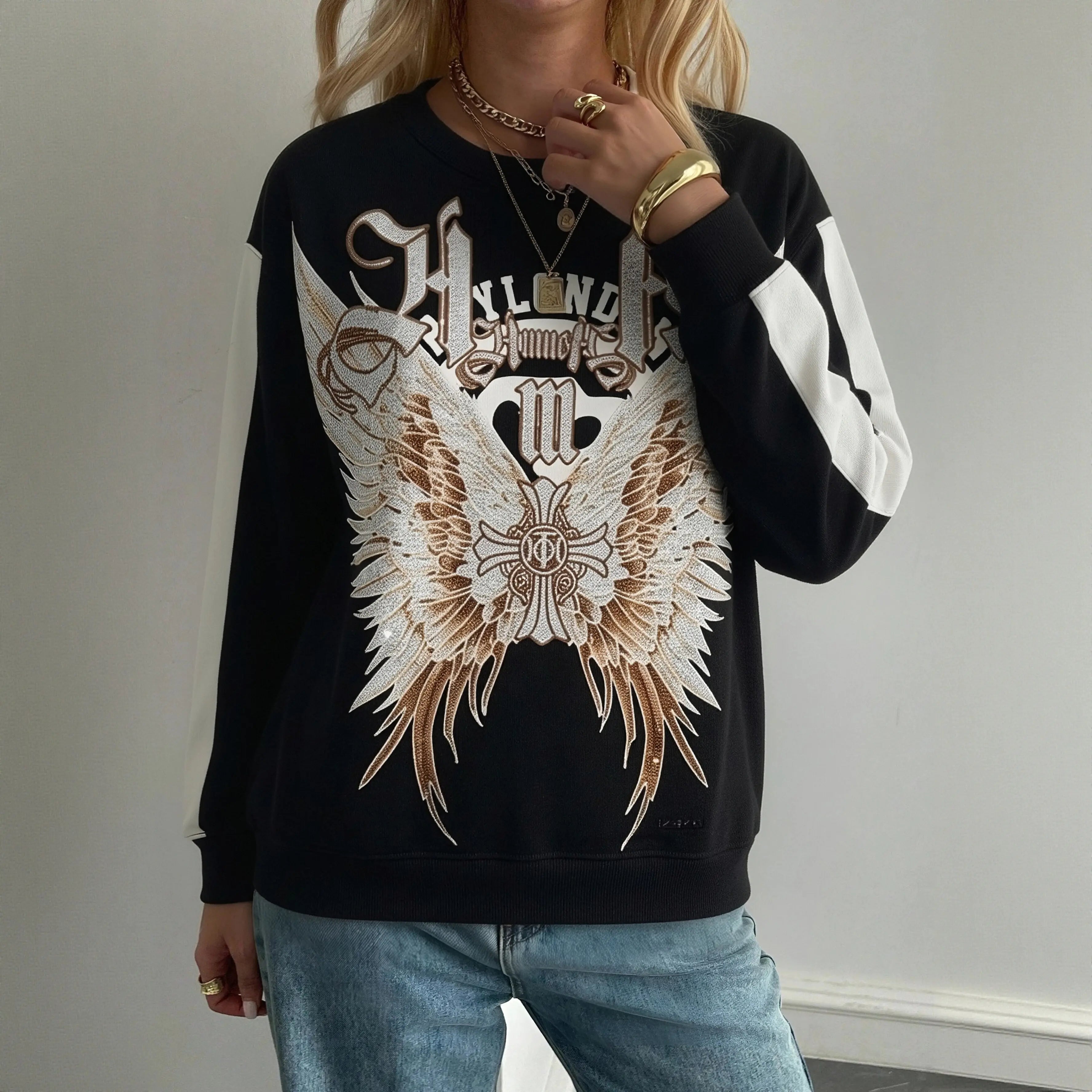 Person wearing a black sweatshirt with a large graphic design on a plain background， TCH Rhinestone Wing M Embroidered Sweatshirt